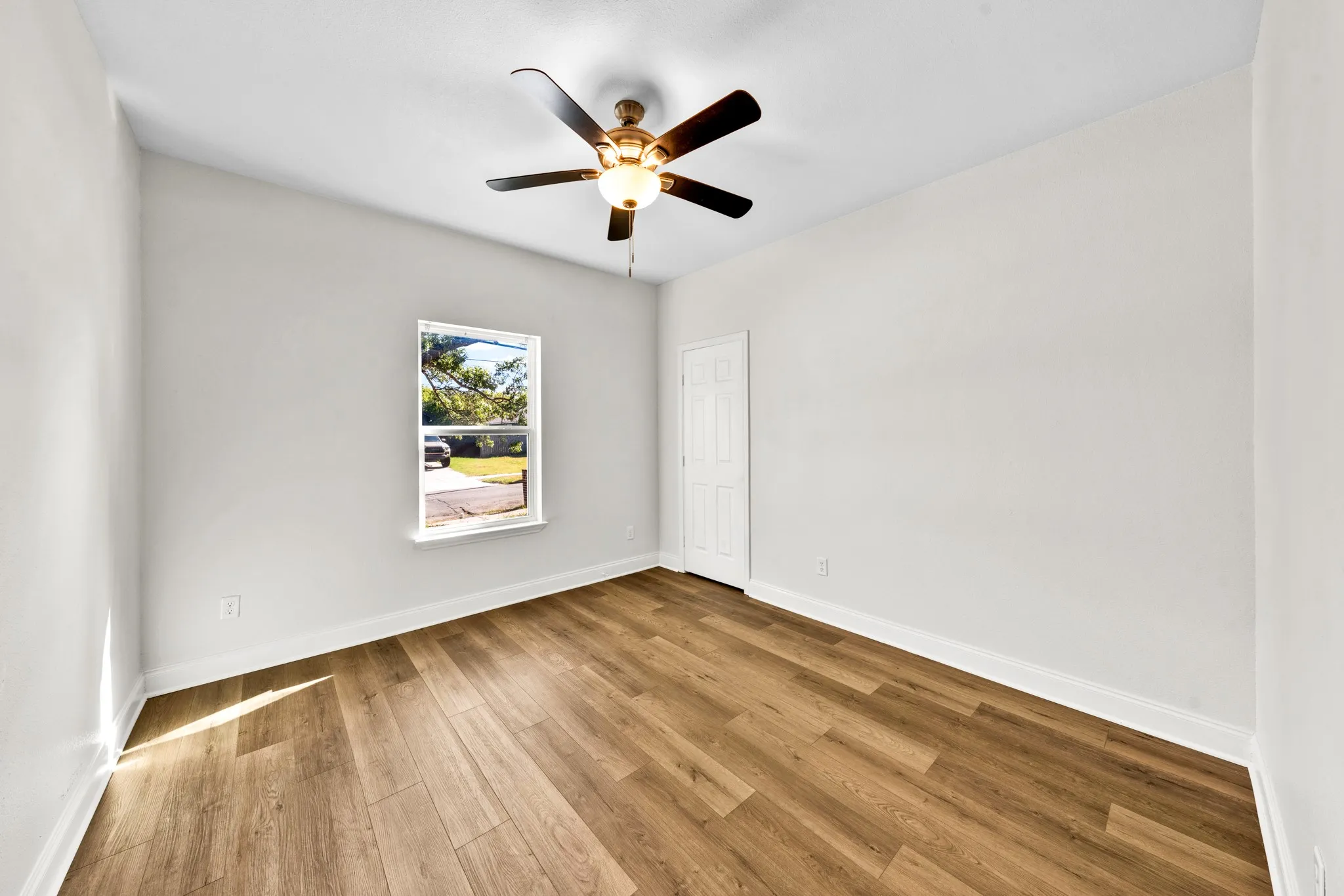 Wood-finish flooring, a ceiling fan with integrated lighting, and a single window