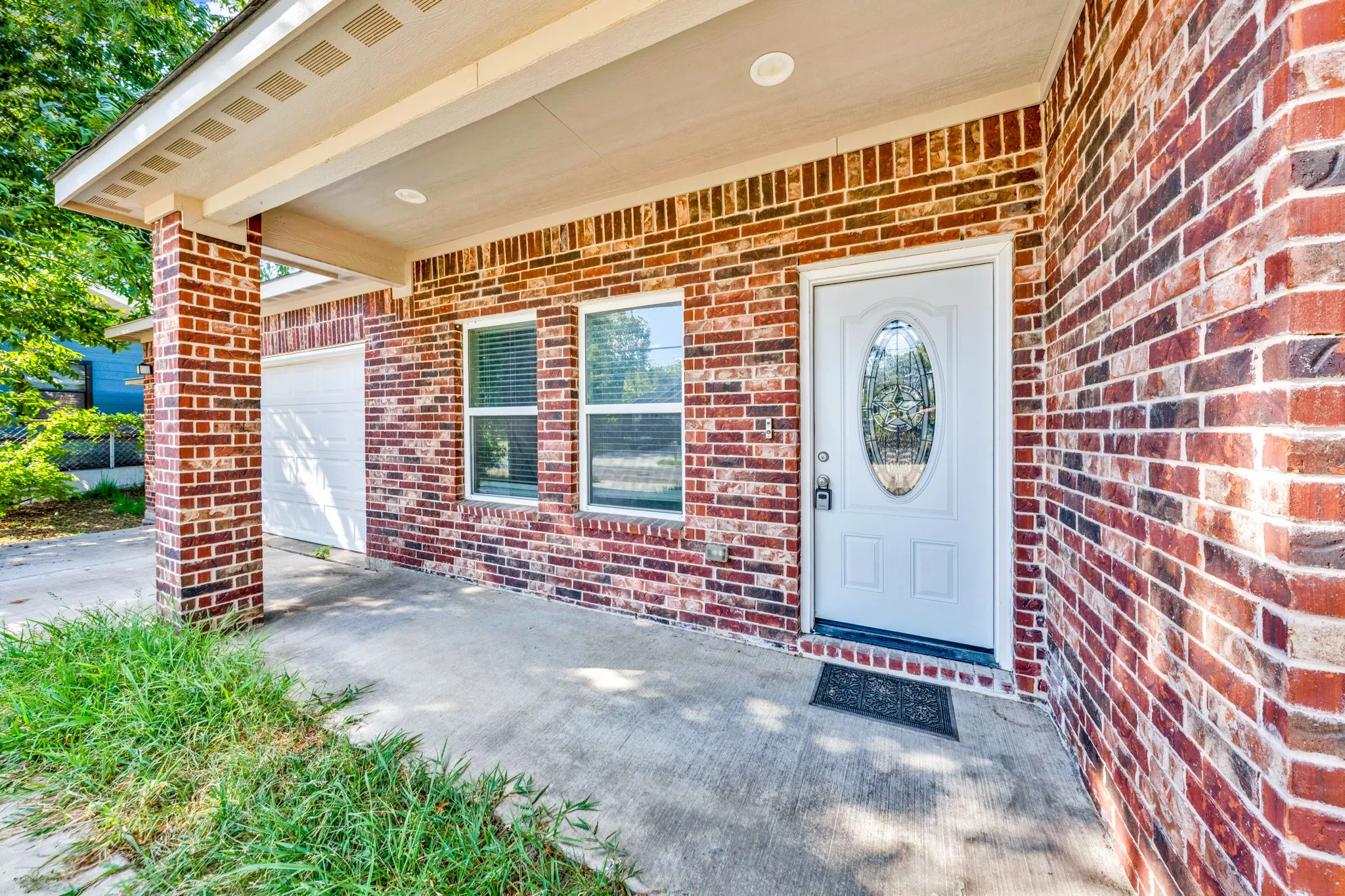 Brick exterior with a covered porch, white entry door with an oval glass insert, and two windows with blinds
