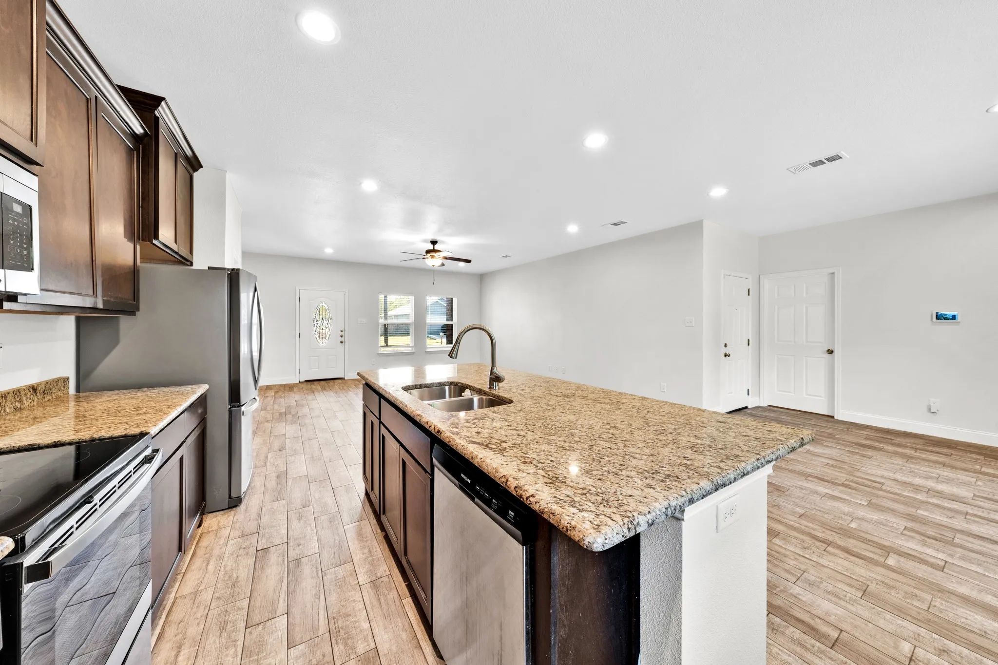 Kitchen featuring wood-finish cabinetry, granite countertops, stainless steel appliances, and a central island with a double sink