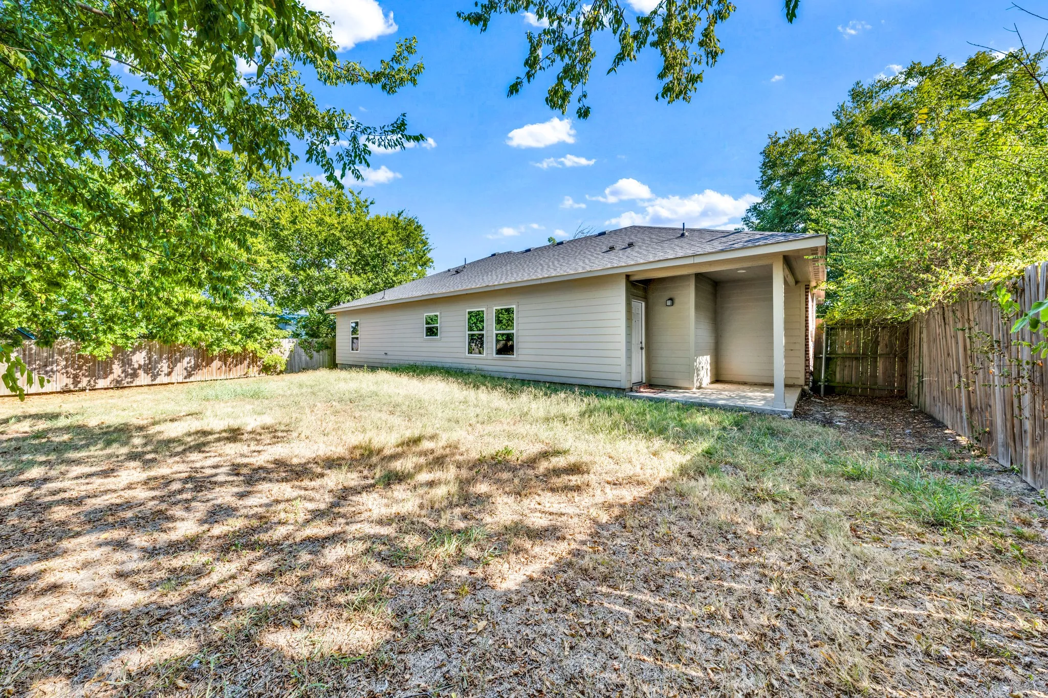 Expansive backyard featuring a covered patio, privacy fencing, and mature trees