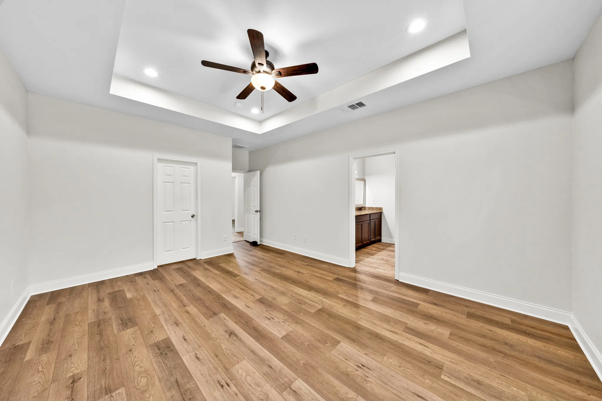 Tray ceiling with recessed lighting, wood-finish flooring, ceiling fan with light, and white paneled doors