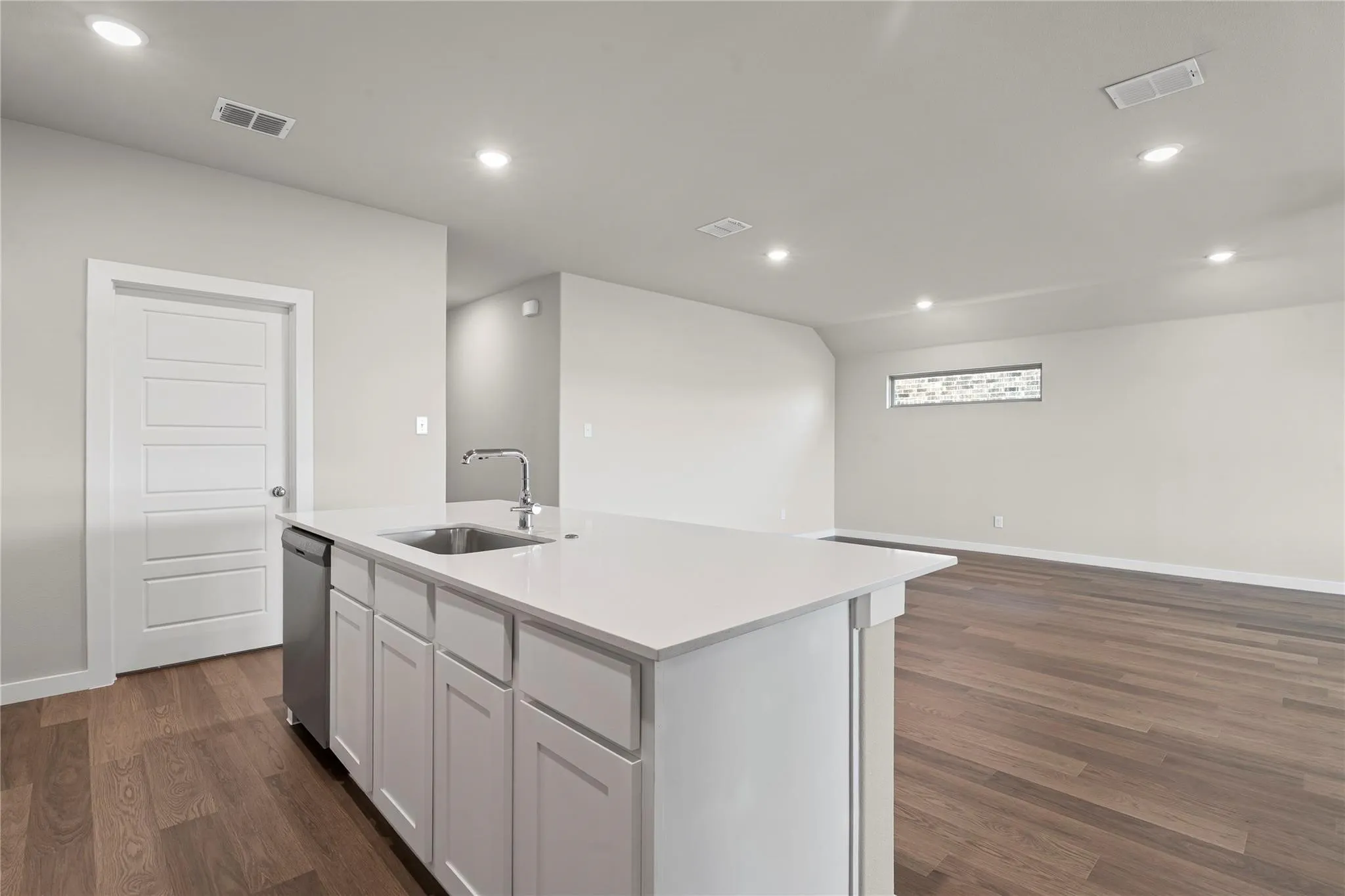 Kitchen island with an undermount sink and chrome faucet, white cabinetry, a built-in dishwasher, and wood-finish flooring