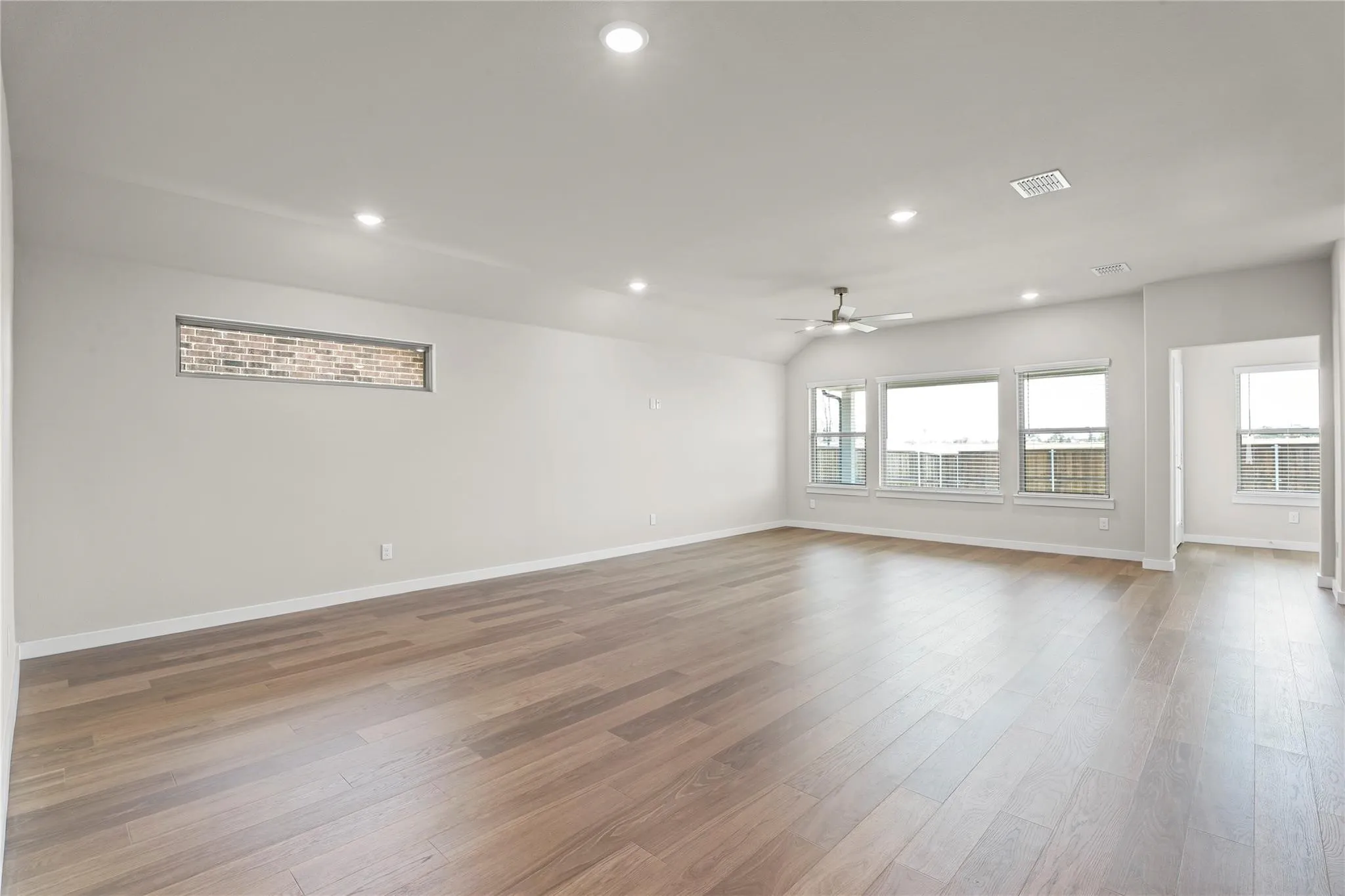 Spacious room featuring wood-finish flooring, recessed lighting, a ceiling fan, and multiple windows