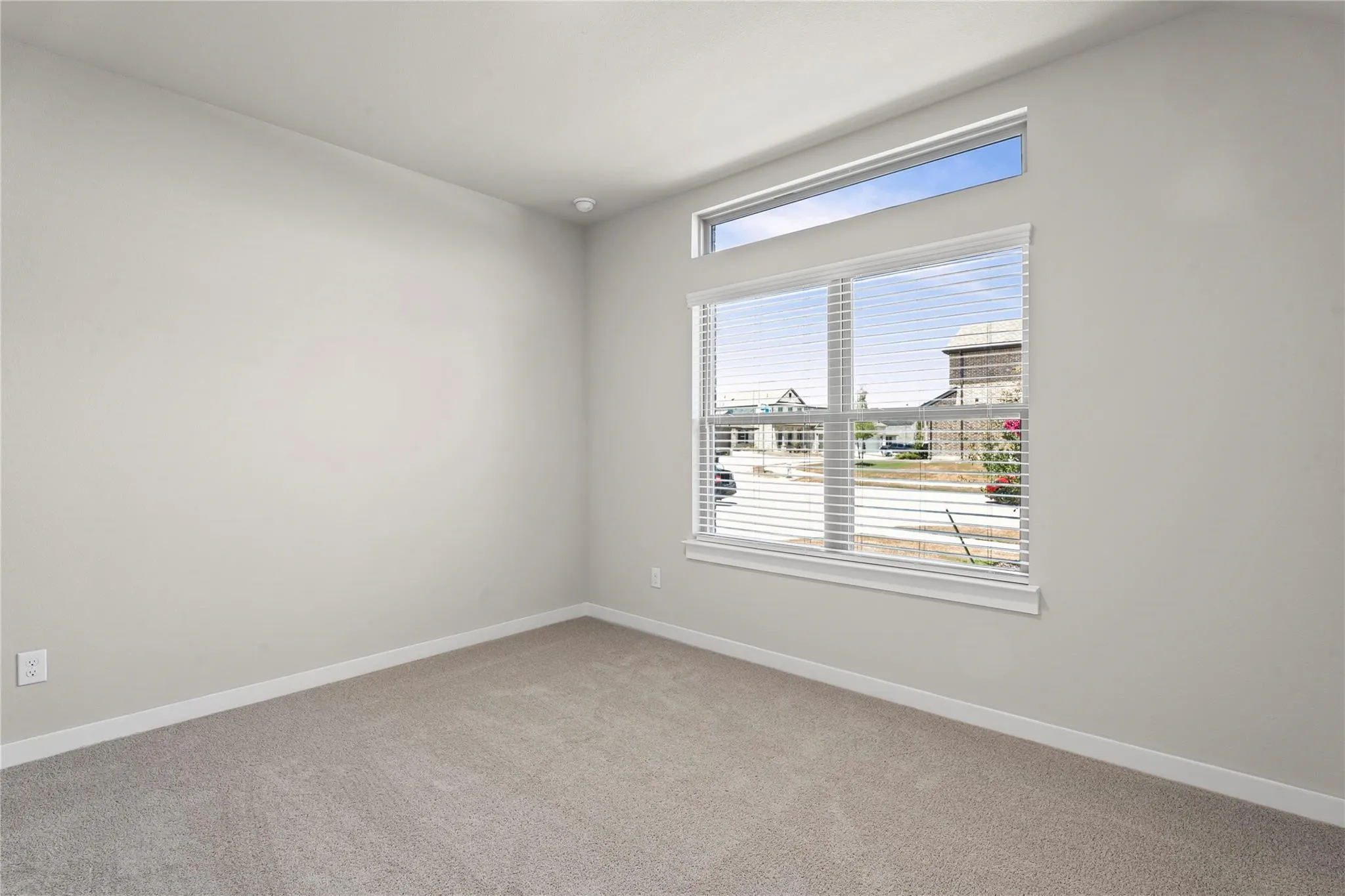 Bright corner bedroom featuring neutral carpet flooring, pristine white walls, and expansive windows with horizontal blinds flooding the space with natural light