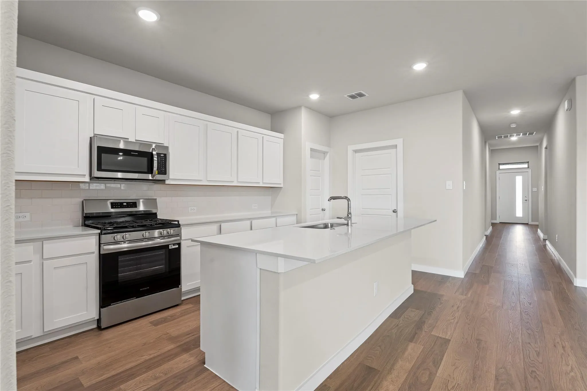 Kitchen featuring white cabinetry, stainless steel appliances, a center island with sink, and wood-finish flooring