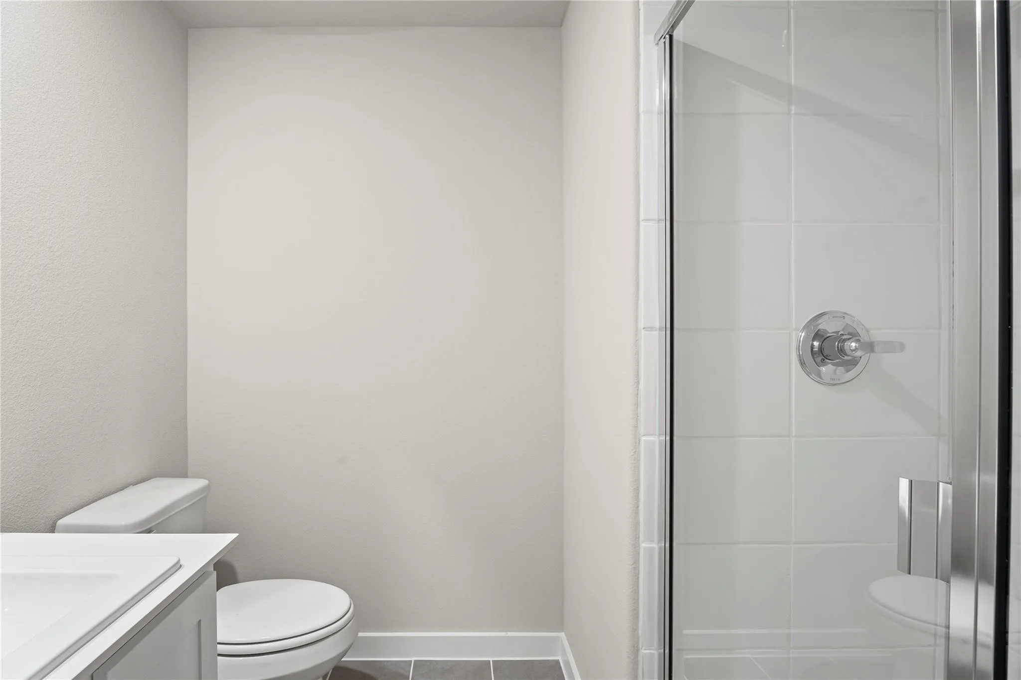 Full bathroom featuring a glass-enclosed shower with white subway tile, a white toilet, and a vanity with a white countertop