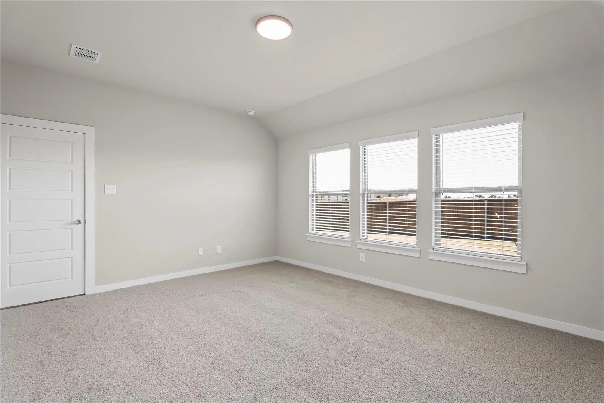 Soft grey wall paint, plush carpeting, three large windows, venetian blinds, and a white paneled door