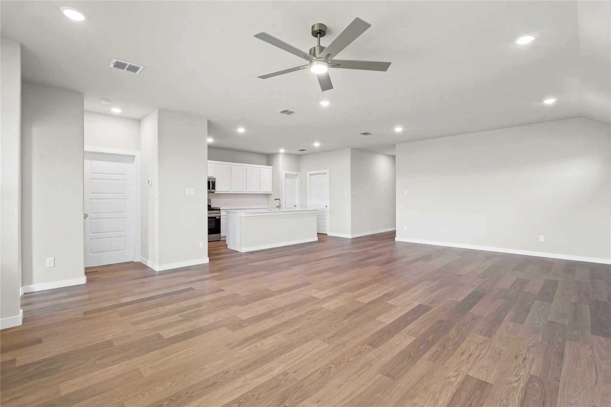 Expansive open-concept living area with wood-finish flooring, recessed lighting, and a contemporary ceiling fan