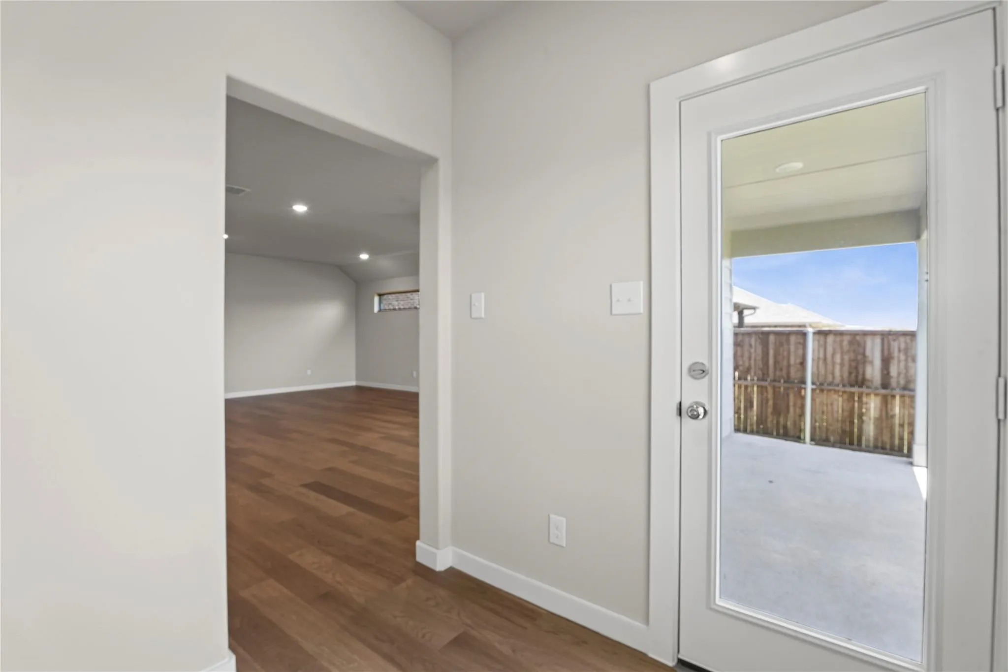 Wood-finish flooring throughout, recessed lighting, and a glass-paneled door opening to a concrete patio