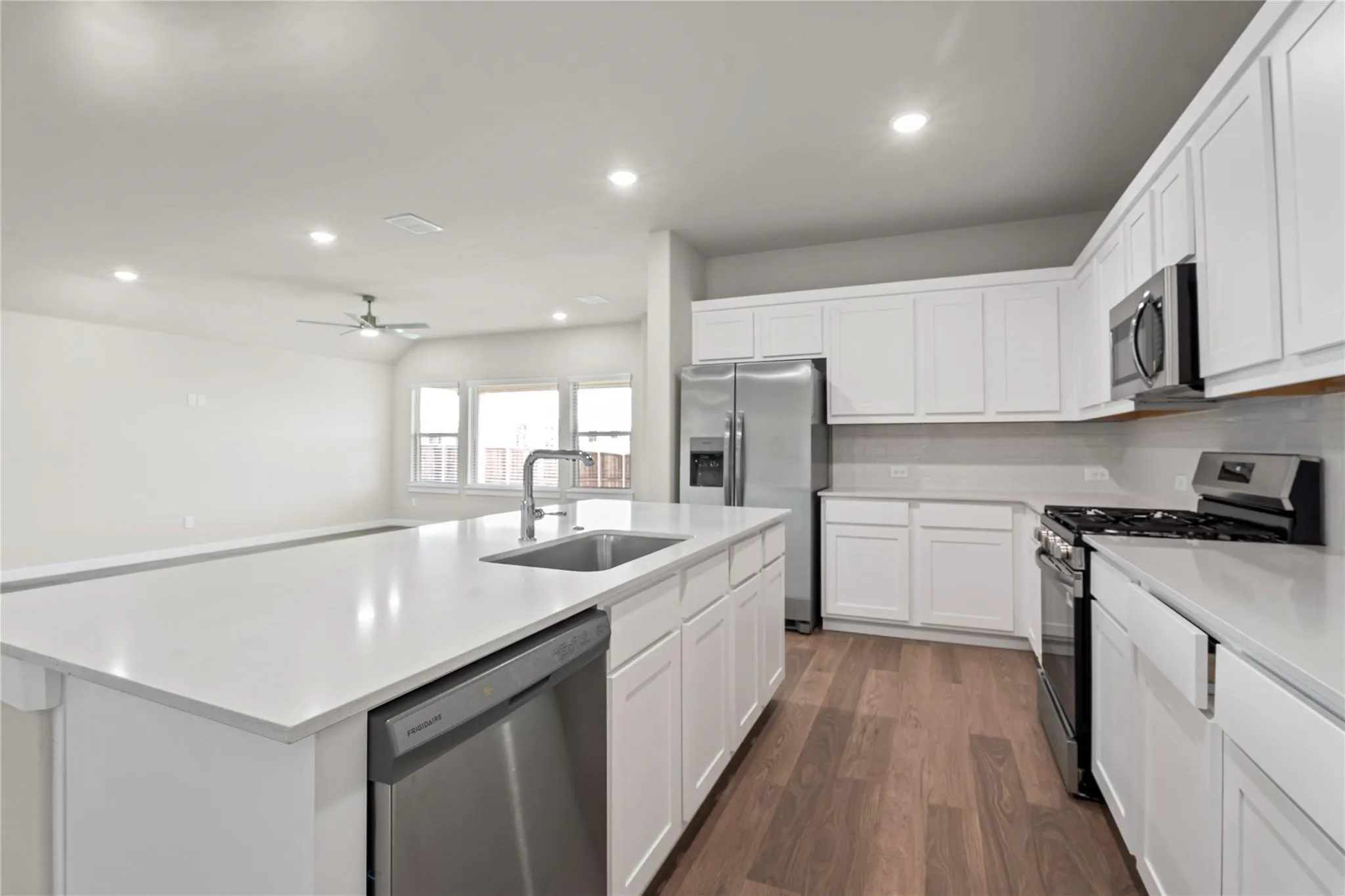 Kitchen featuring an expansive island with an undermount sink, stainless steel appliances, white cabinetry, and wood-finish flooring
