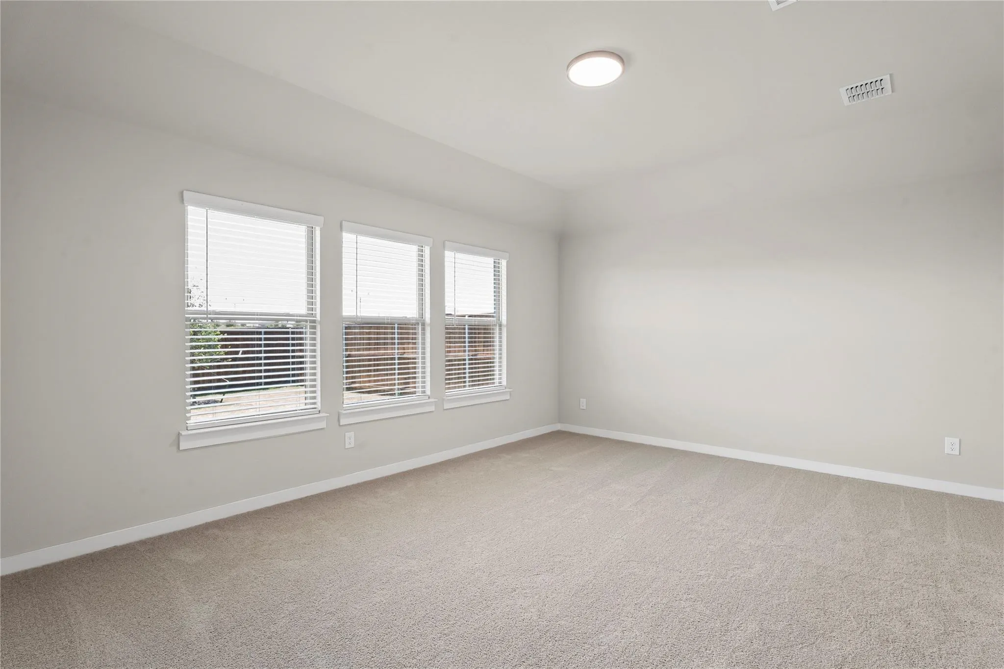 Neutral-toned carpeted flooring, three windows with white blinds, and a flush-mount ceiling light fixture