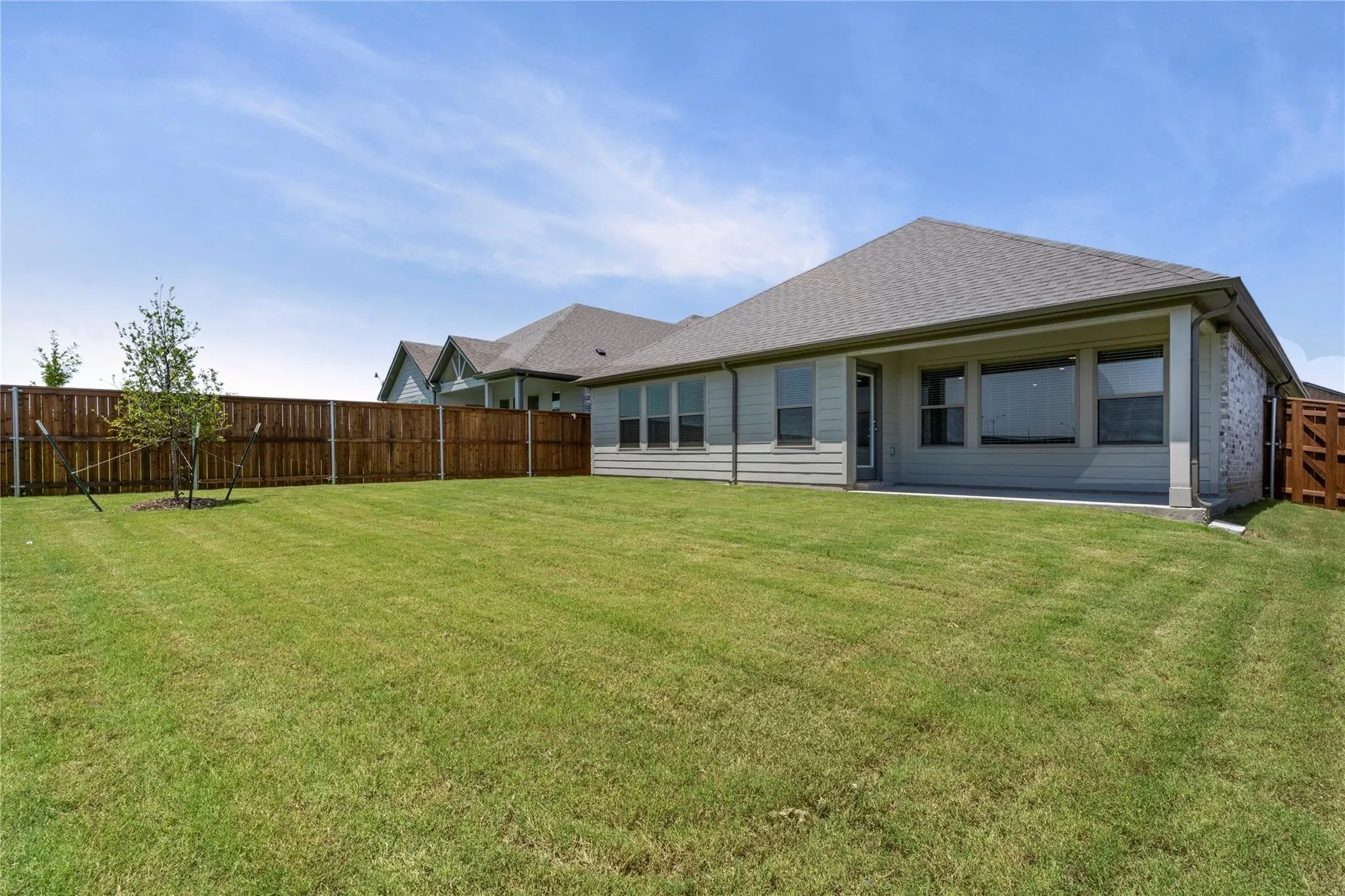 Expansive backyard featuring a manicured lawn, wood privacy fencing, a covered concrete patio, and a light-colored exterior with multiple windows