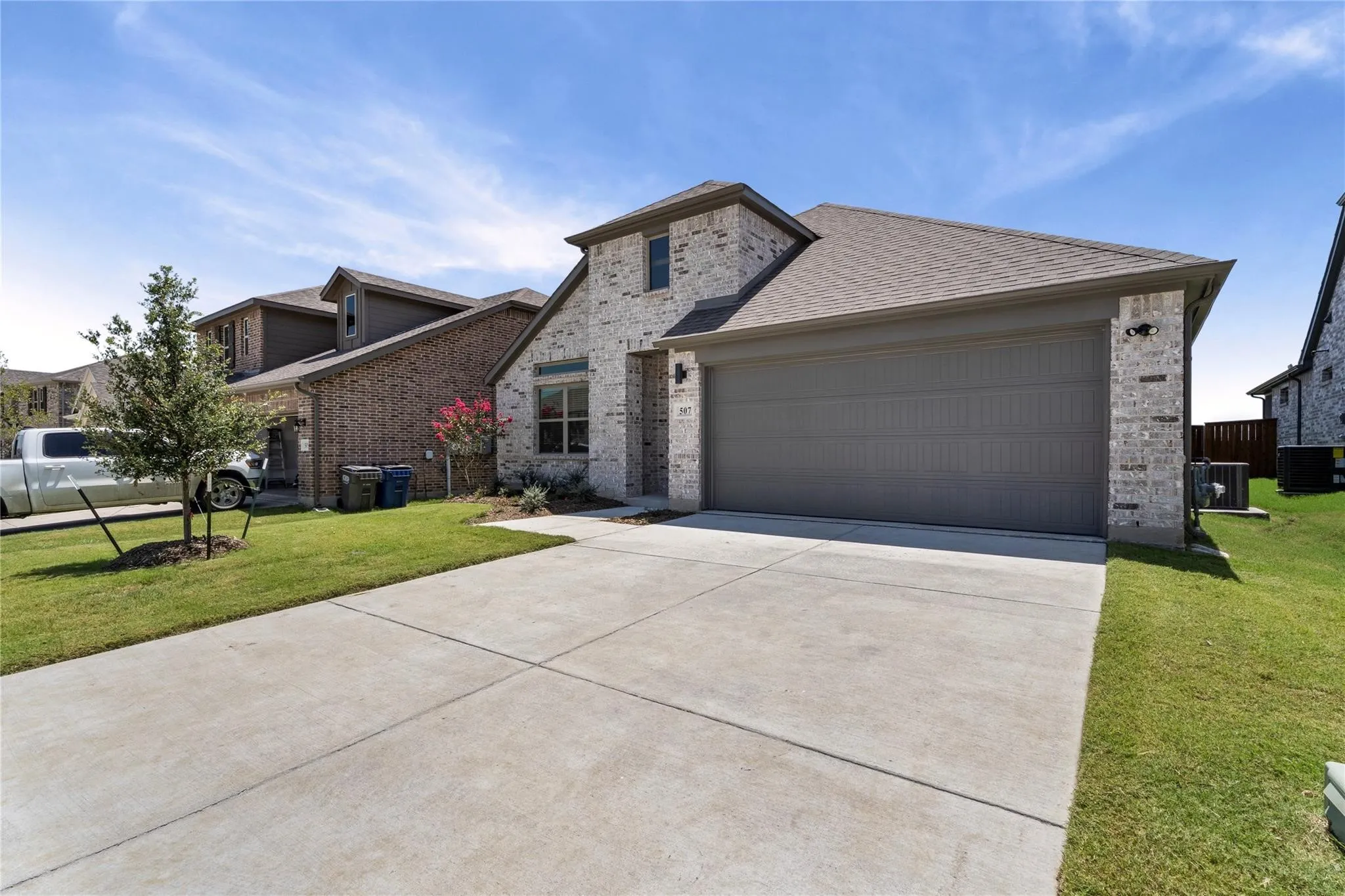 Stone and brick exterior with a gray garage door, concrete driveway, and established landscaping