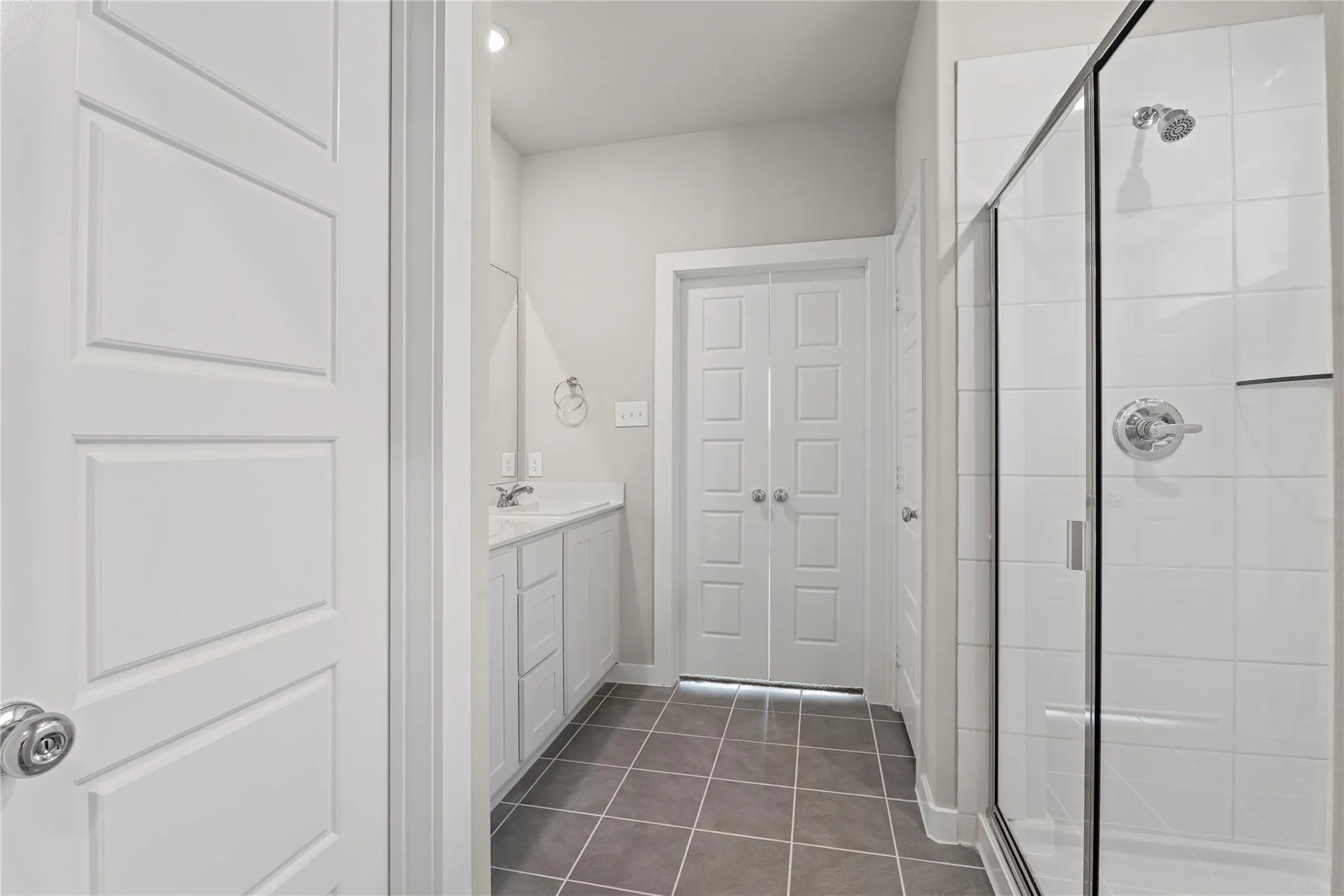 Modern bathroom featuring a glass-enclosed shower with subway tile, white vanity with integrated sink, and gray tiled flooring