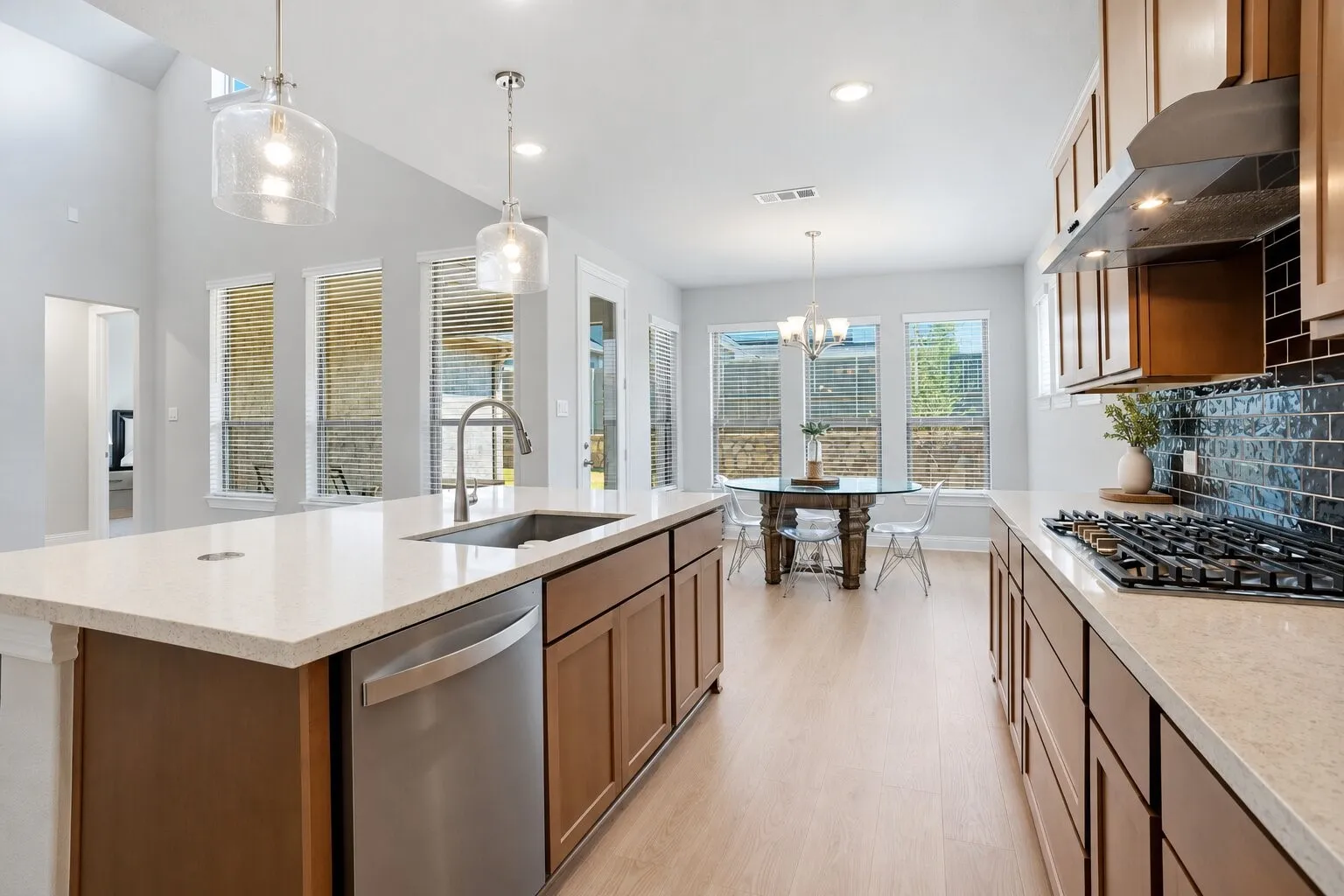 Bright, open kitchen with an oversized island, gas cooktop, abundant cabinetry, and a sun-filled dining area surrounded by windows. Photos have been AI enhanced for presentation; no material property features were altered.