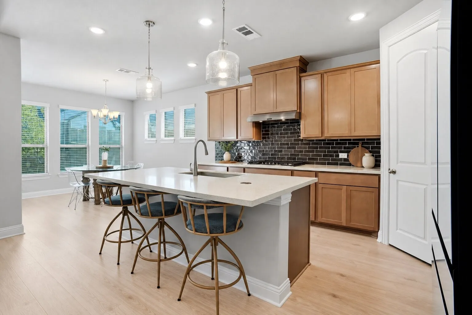 Spacious kitchen with an oversized island, seating for three, abundant cabinetry, gas cooktop, walk-in pantry, and an adjacent sunlit dining area. Photos have been AI enhanced for presentation; no material property features were altered.