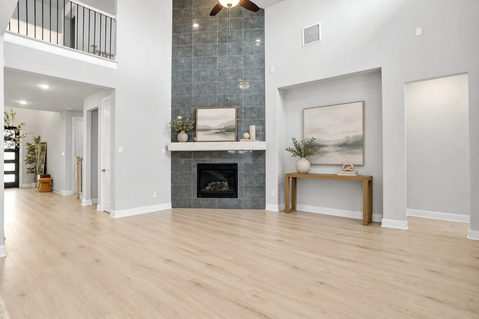Spacious living room with soaring 20-foot ceilings, an impressive floor-to-ceiling tiled fireplace, abundant natural light, and an open view to the upstairs loft. Photos have been AI enhanced for presentation; no material property features were altered.