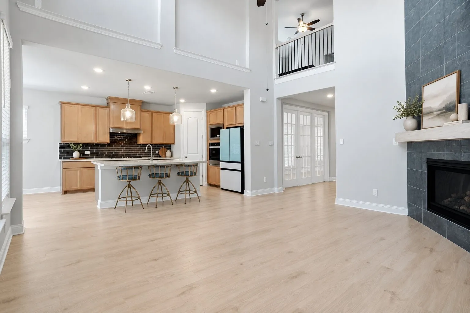 Open-concept living and kitchen area with soaring 20-foot ceilings, a statement fireplace, spacious island seating, and an upstairs overlook. Photos have been AI enhanced for presentation; no material property features were altered.