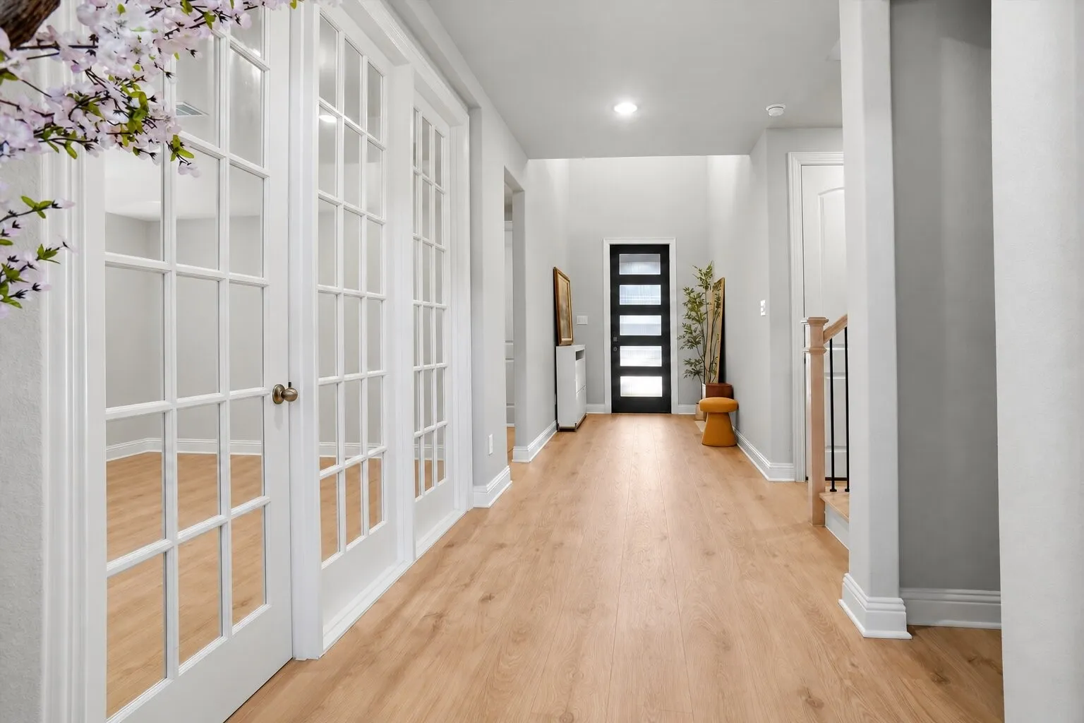Welcoming entry with light wood flooring and French doors opening to a versatile office that can also serve as a sitting room, second living area, or formal dining room. Photos have been AI enhanced for presentation; no material property features were altered.
