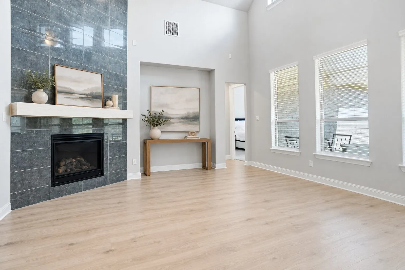 Expansive living room with 20-foot ceilings, a dramatic floor-to-ceiling tiled fireplace, and tall windows that fill the space with natural light. Photos have been AI enhanced for presentation; no material property features were altered.