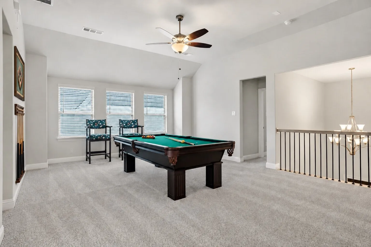 Spacious upstairs game room with a vaulted ceiling, abundant natural light, and an open overlook to the main level; pool table and chairs convey with the home. Photos have been AI enhanced for presentation; no material property features were altered.