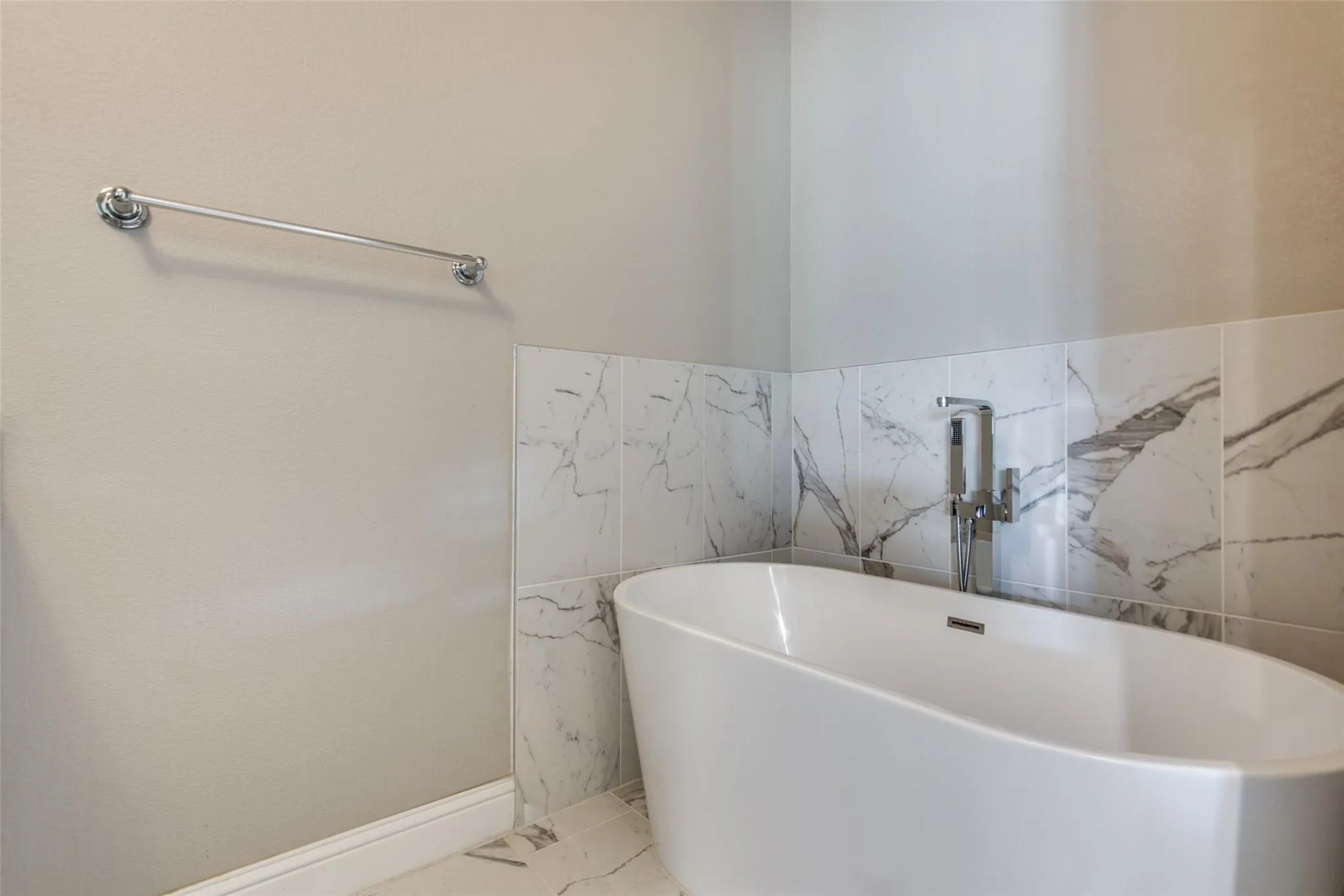 Freestanding soaking tub with chrome fixtures, surrounded by large format tile with natural stone-look veining