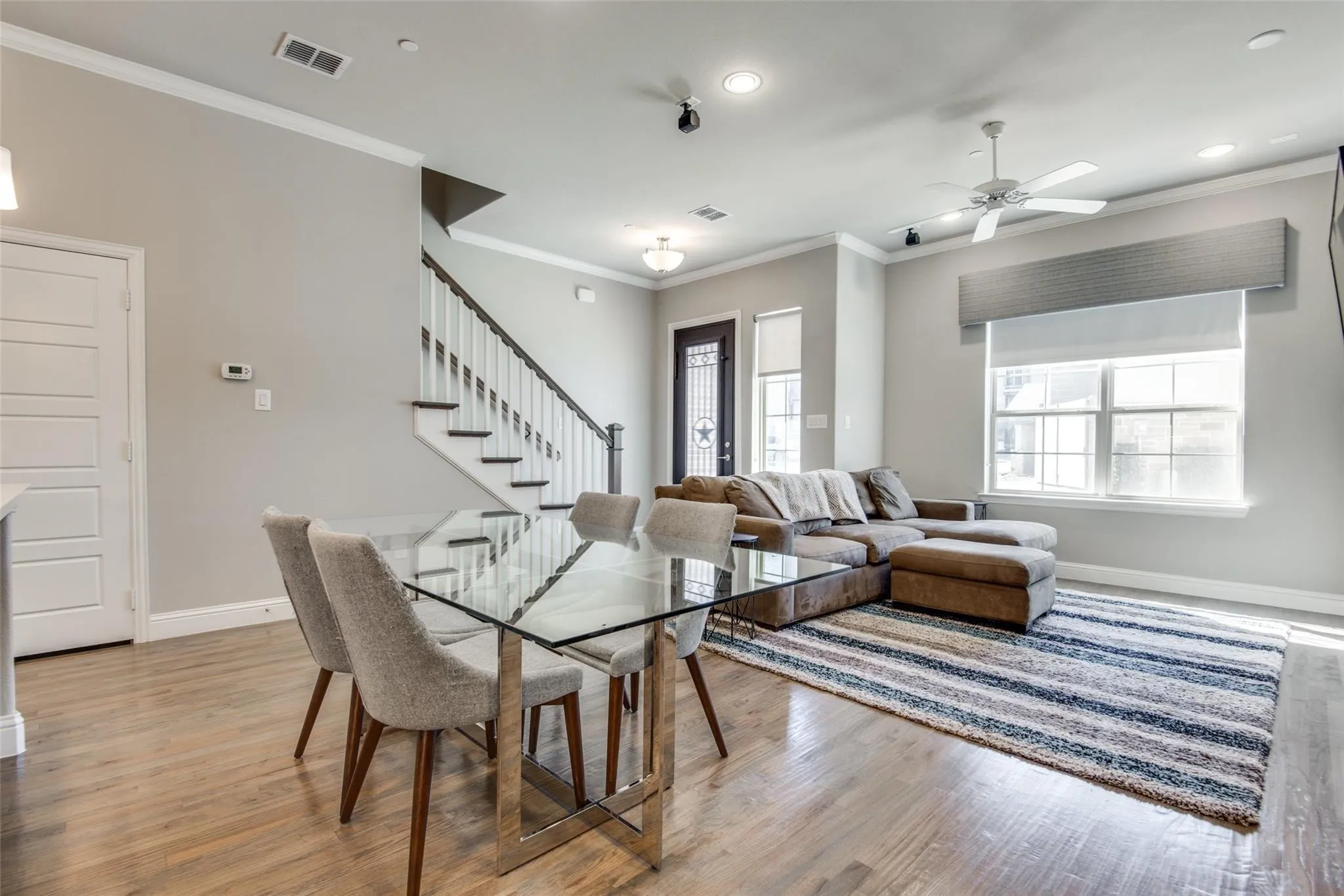 Wood-finish flooring throughout, featuring a staircase with white risers and dark wood handrails, recessed lighting, and a ceiling fan