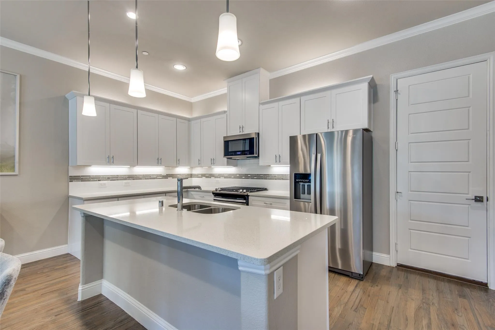 Kitchen featuring stainless steel appliances, white cabinetry, a large center island with a double sink, and wood-finish flooring
