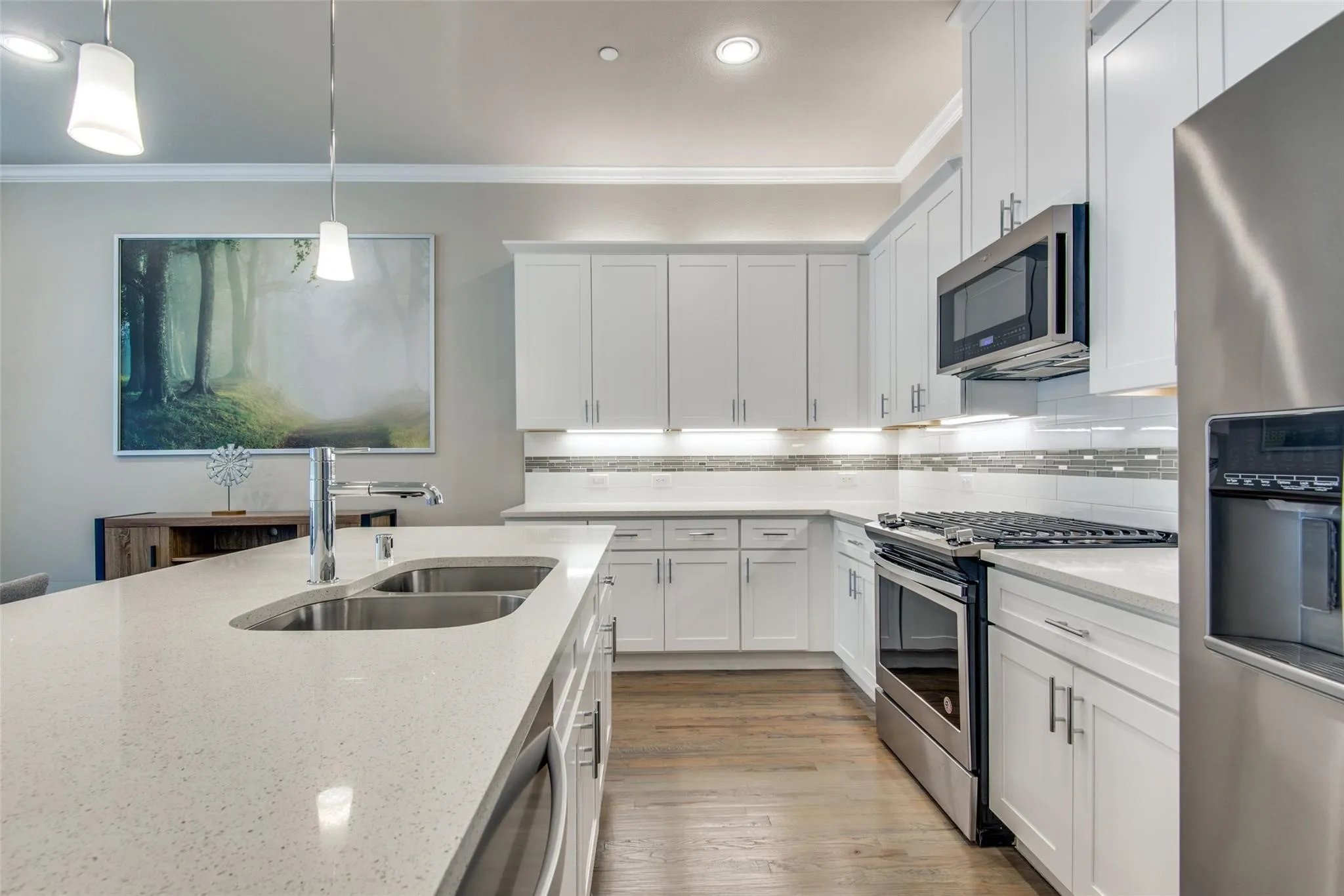 Kitchen featuring white cabinetry, stainless steel appliances, a double basin undermount sink, pendant lighting, and wood-finish flooring