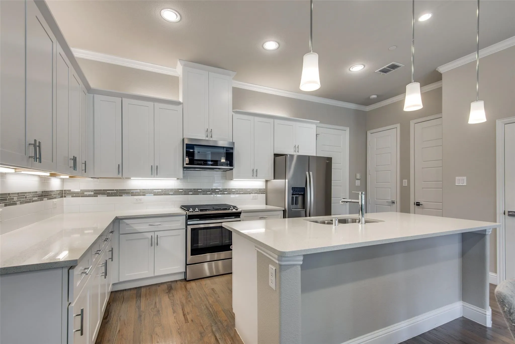 Contemporary kitchen featuring white cabinetry, stainless steel appliances, a center island with sink, quartz countertops, and wood-finish flooring