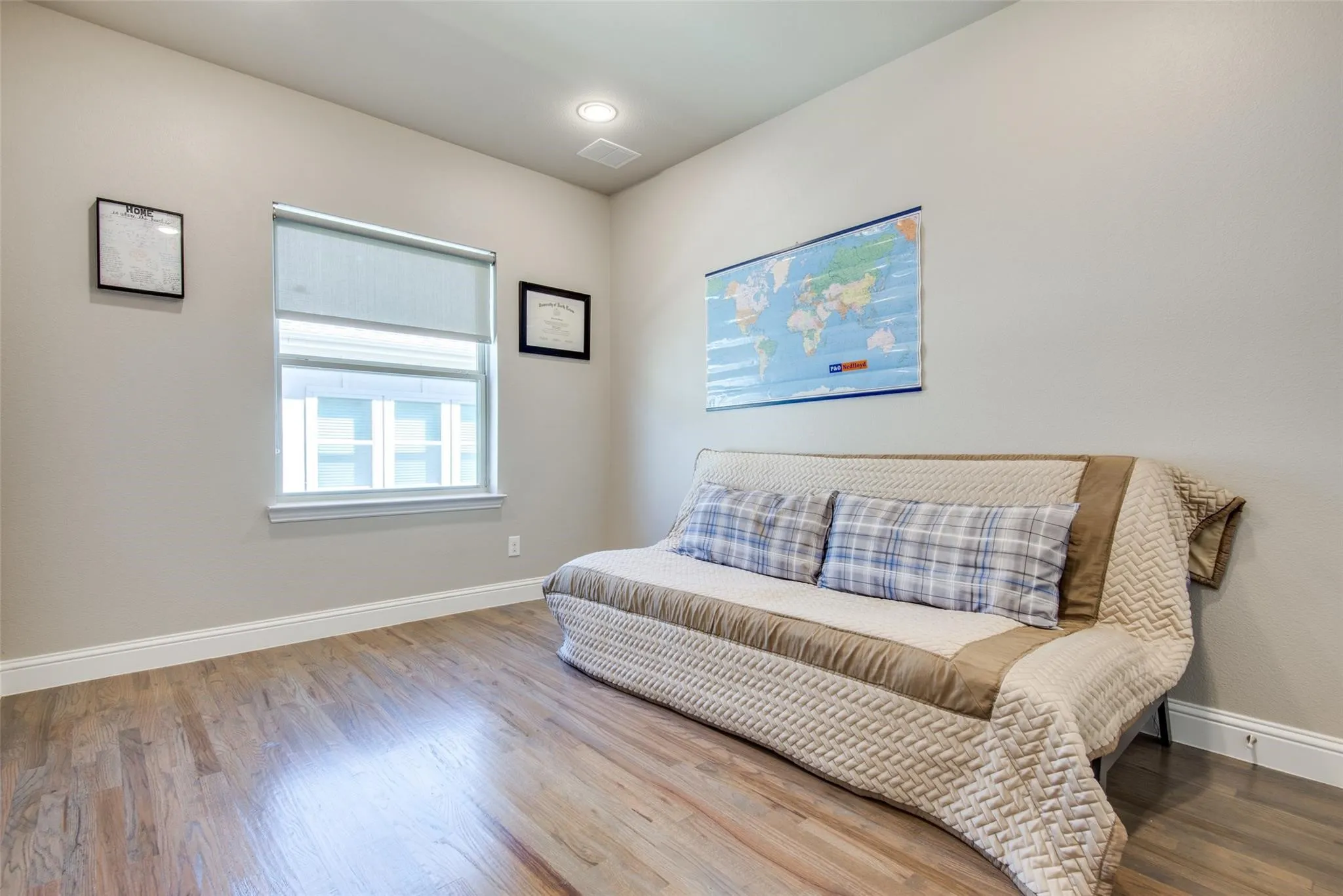 Wood-finish flooring with white trim, recessed lighting, and a single window with a roller shade