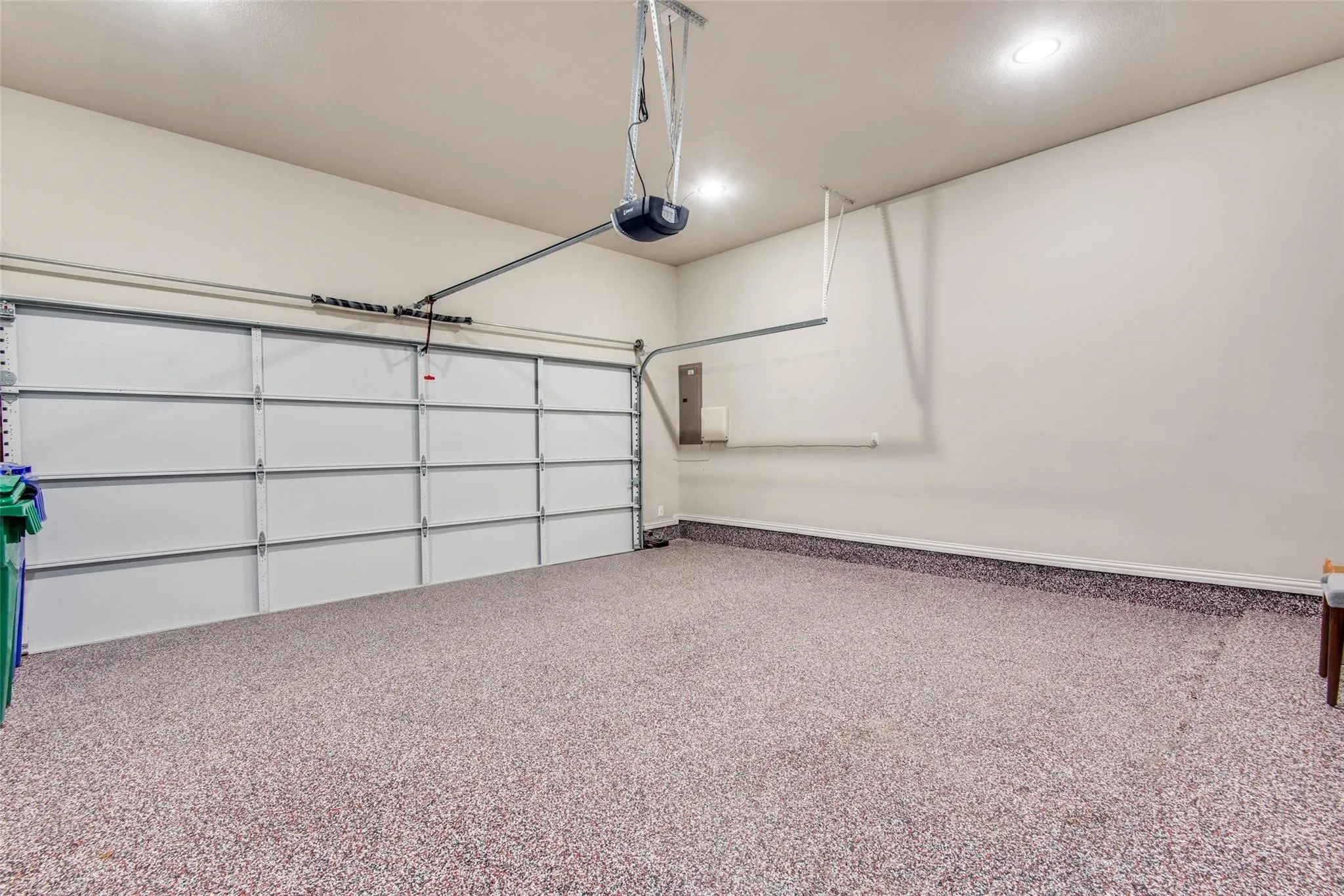 Spacious garage featuring a durable speckled epoxy floor, overhead lighting, and an automated garage door opener system