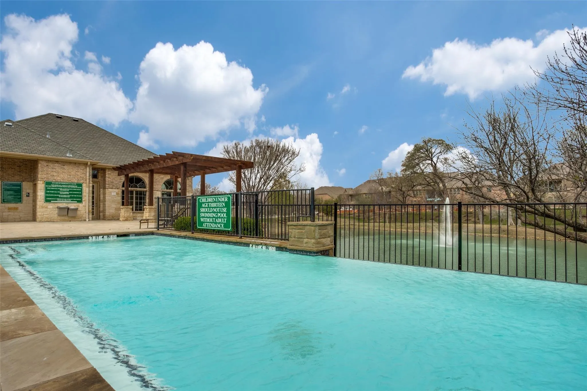Swimming pool with stone coping, adjacent to a brick building with arched windows, and a wooden pergola