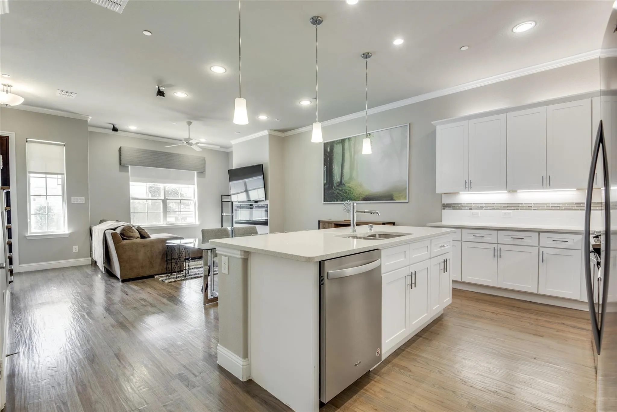 Open-concept living space featuring wood-finish flooring, recessed lighting, and a modern kitchen island with an undermount sink