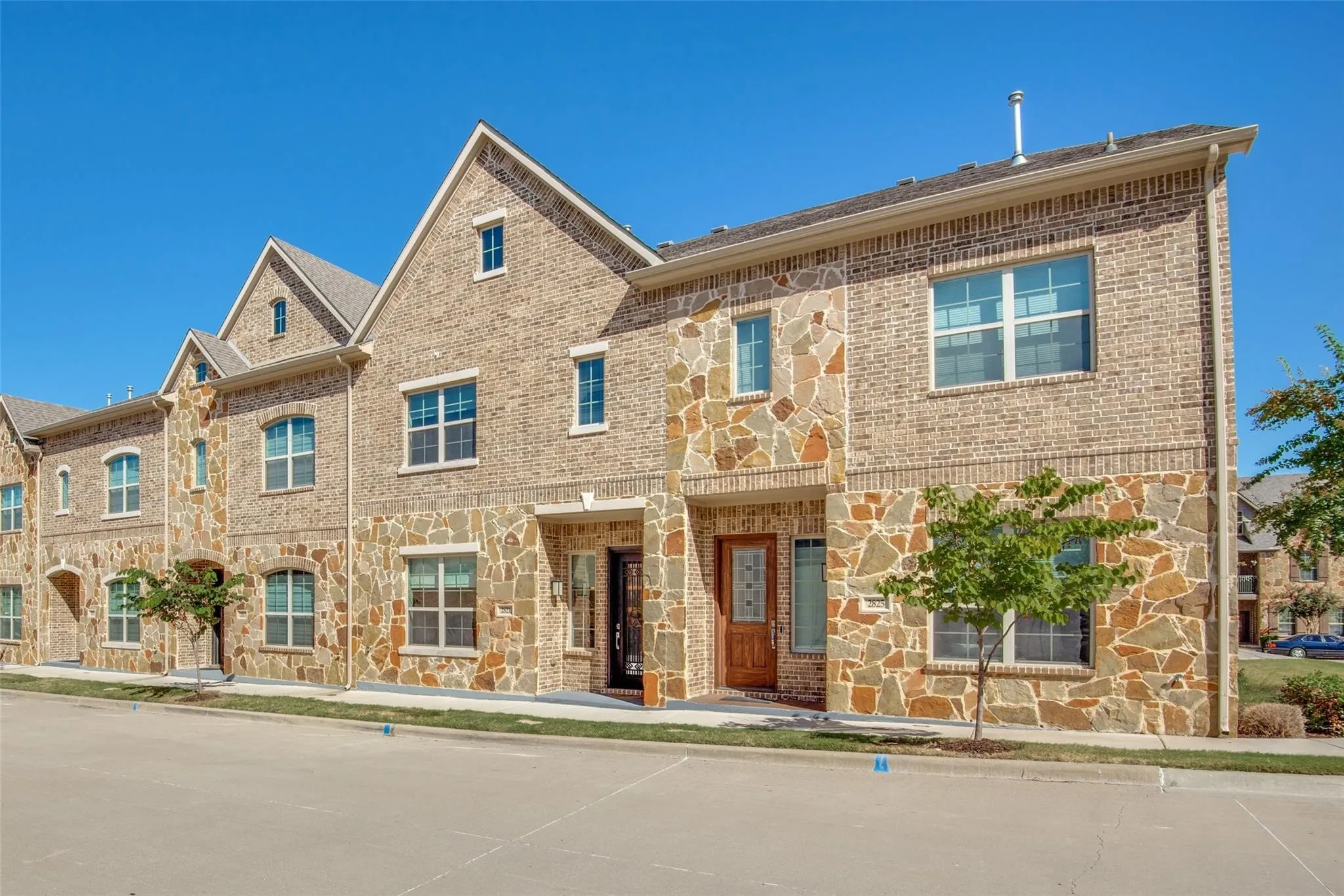 Brick and stone facade townhome featuring multiple gabled rooflines, abundant windows, and a wood-finish entry door