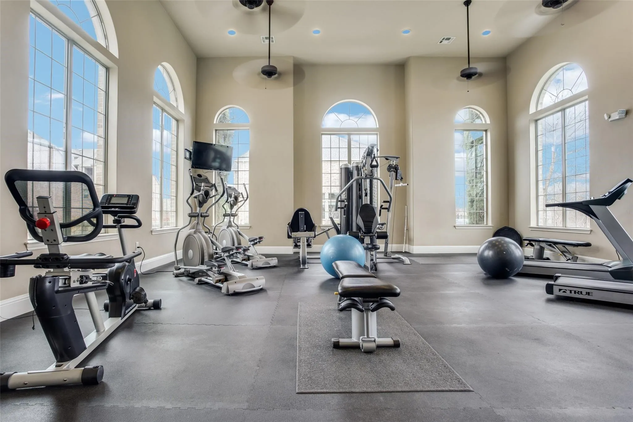 Fitness area featuring multiple arched windows, recessed lighting, ceiling fans, and rubber flooring
