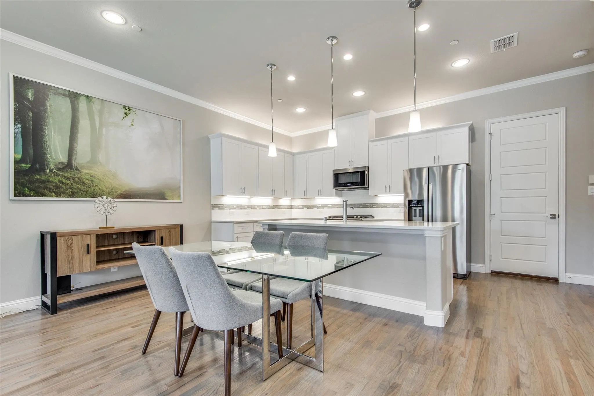 Open-concept kitchen and dining area featuring light wood-finish flooring, white cabinetry, stainless steel appliances, and recessed lighting