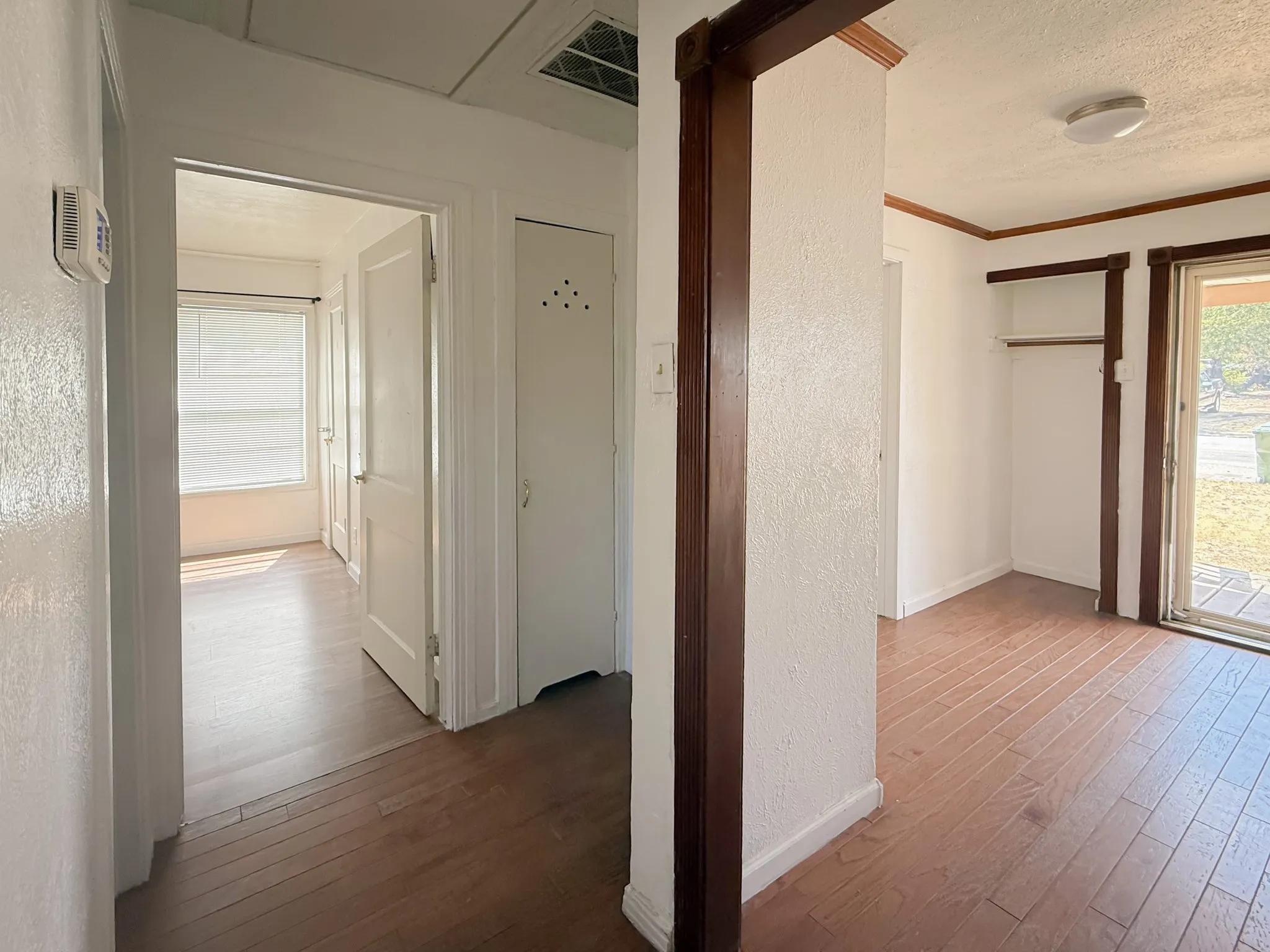 Wood-finish flooring throughout, white painted walls, and built-in closet with hanging rod