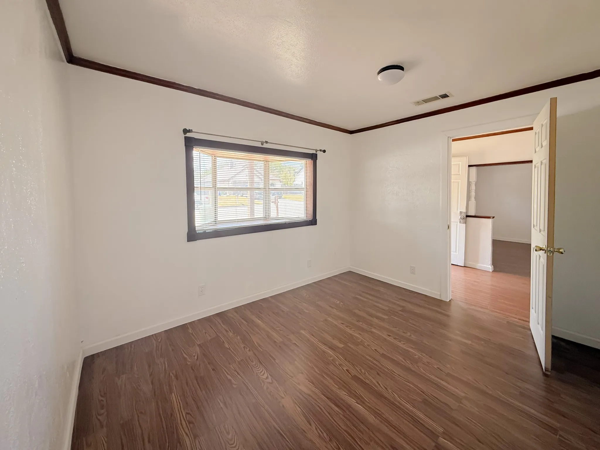 Wood-finish flooring, white walls, dark wood trim, flush mount ceiling light, and natural light from the window