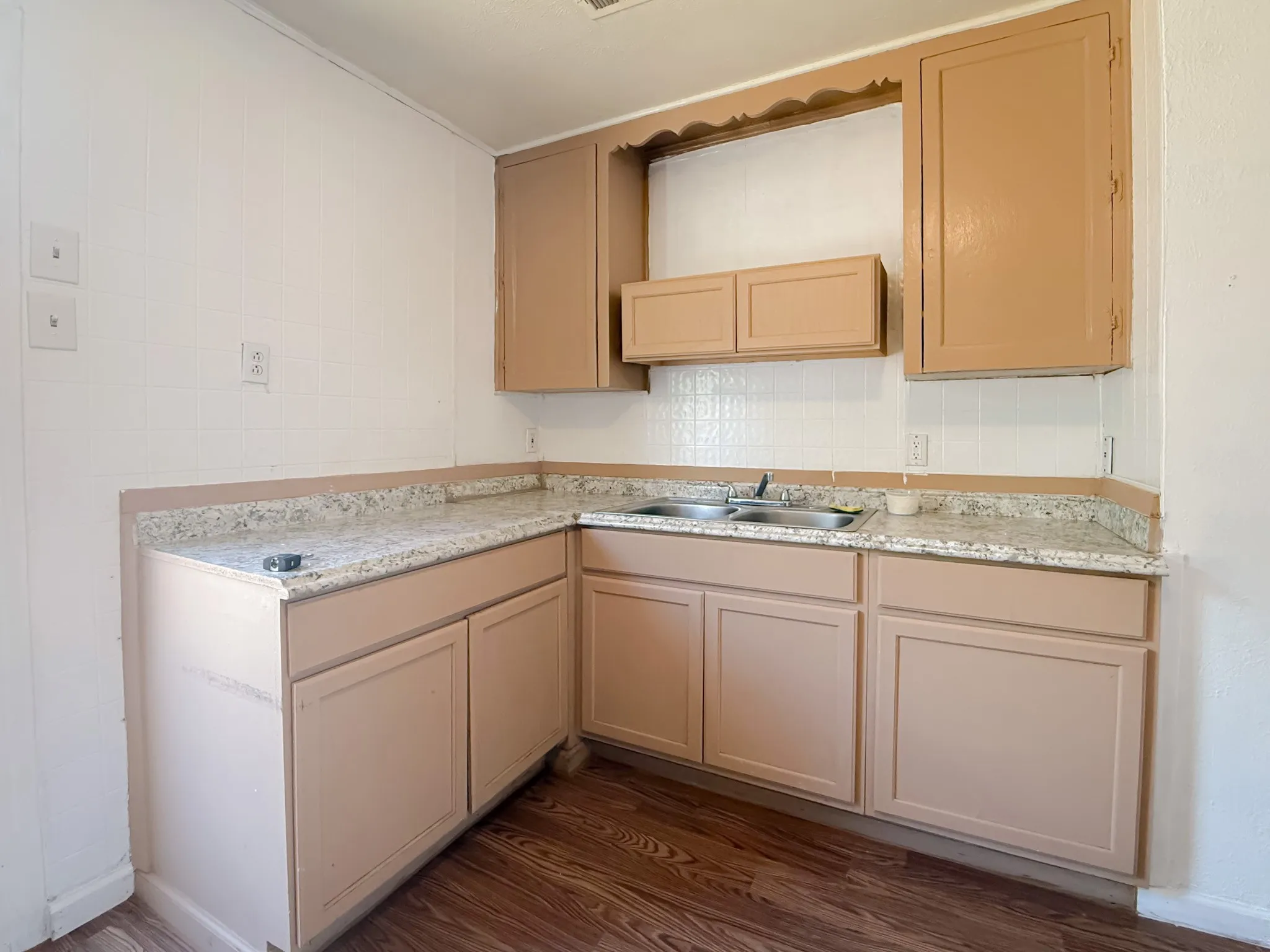 Corner kitchen layout featuring a double basin stainless steel sink, light-toned countertops, wood-finish flooring, and upper and lower cabinetry