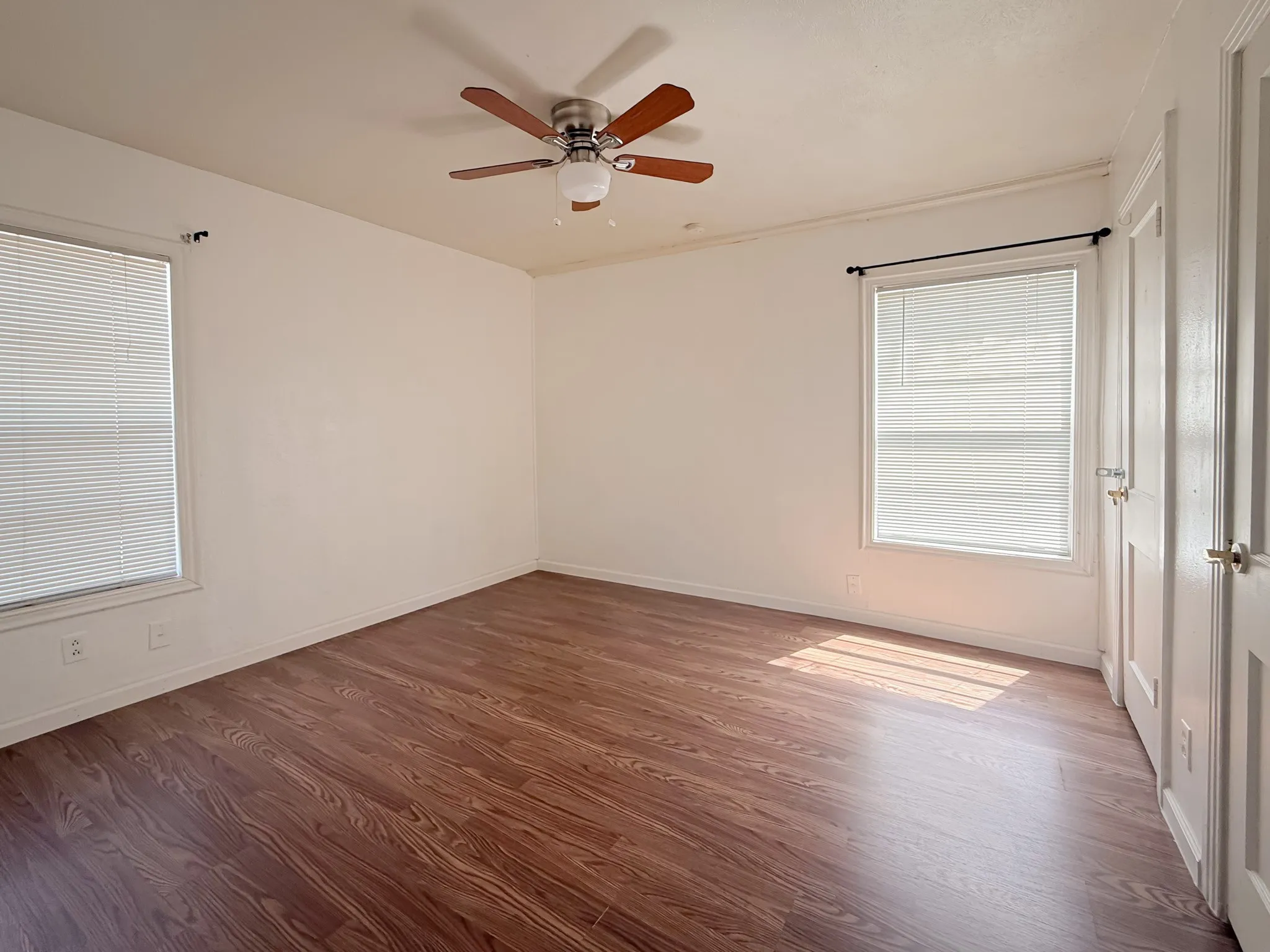 Wood-finish flooring, two windows with blinds, ceiling fan with light fixture, and two panel doors