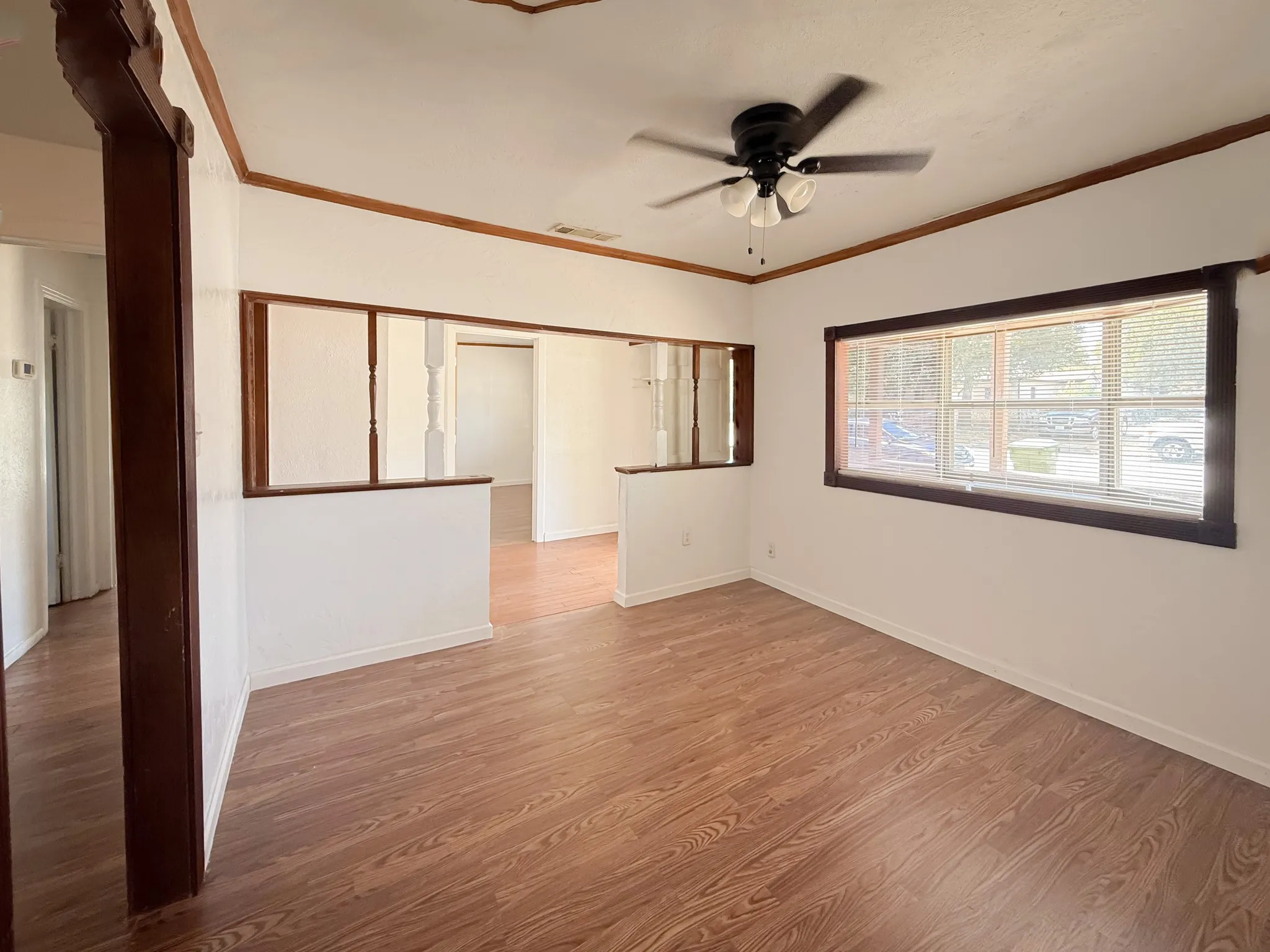 Spacious room featuring wood-finish flooring, a large window, a ceiling fan, and white walls