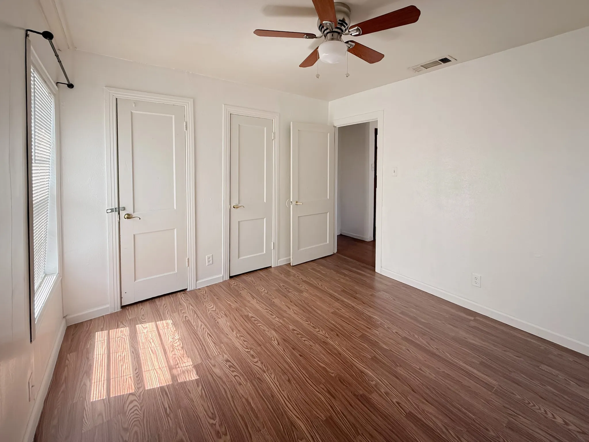 Wood-finish flooring, ceiling fan with light fixture, three panel doors, and window with blinds