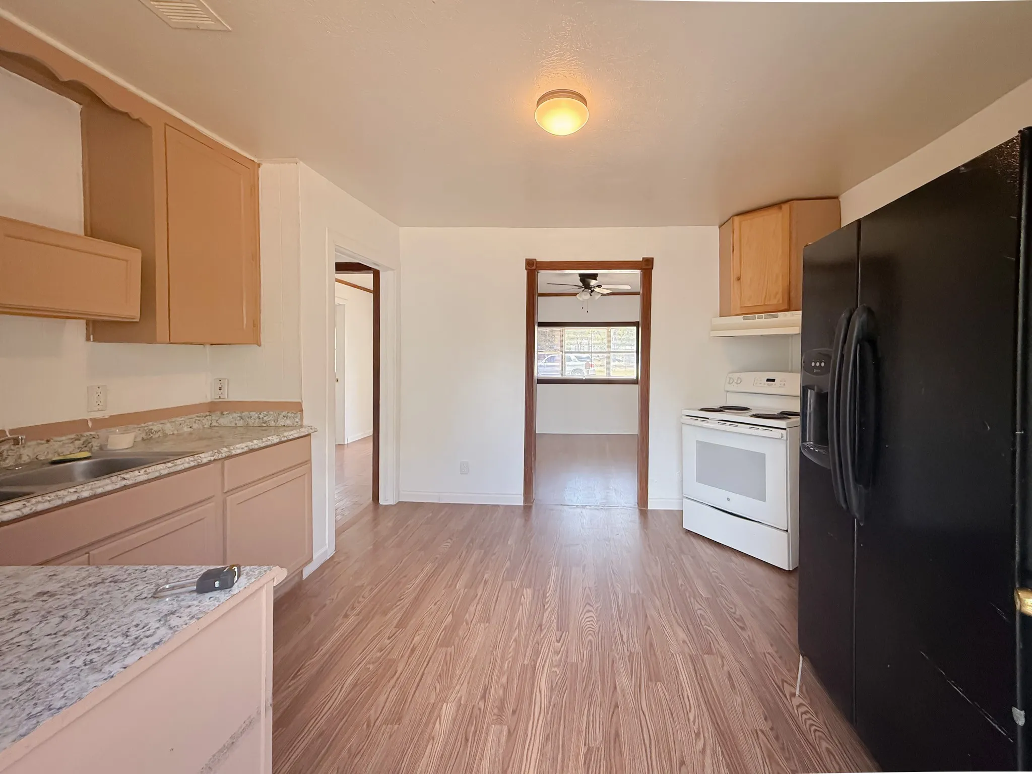 Wood-finish flooring, light wood cabinetry, stone-finish countertops, white electric range, and a black refrigerator
