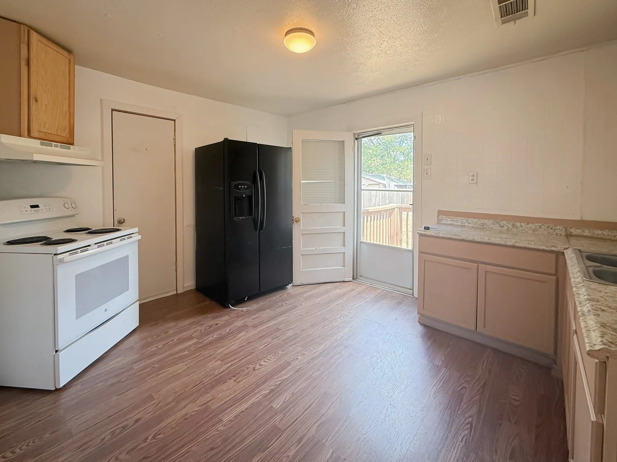 Wood-finish flooring, white range, base cabinetry with light-toned countertops, and a full-size refrigerator