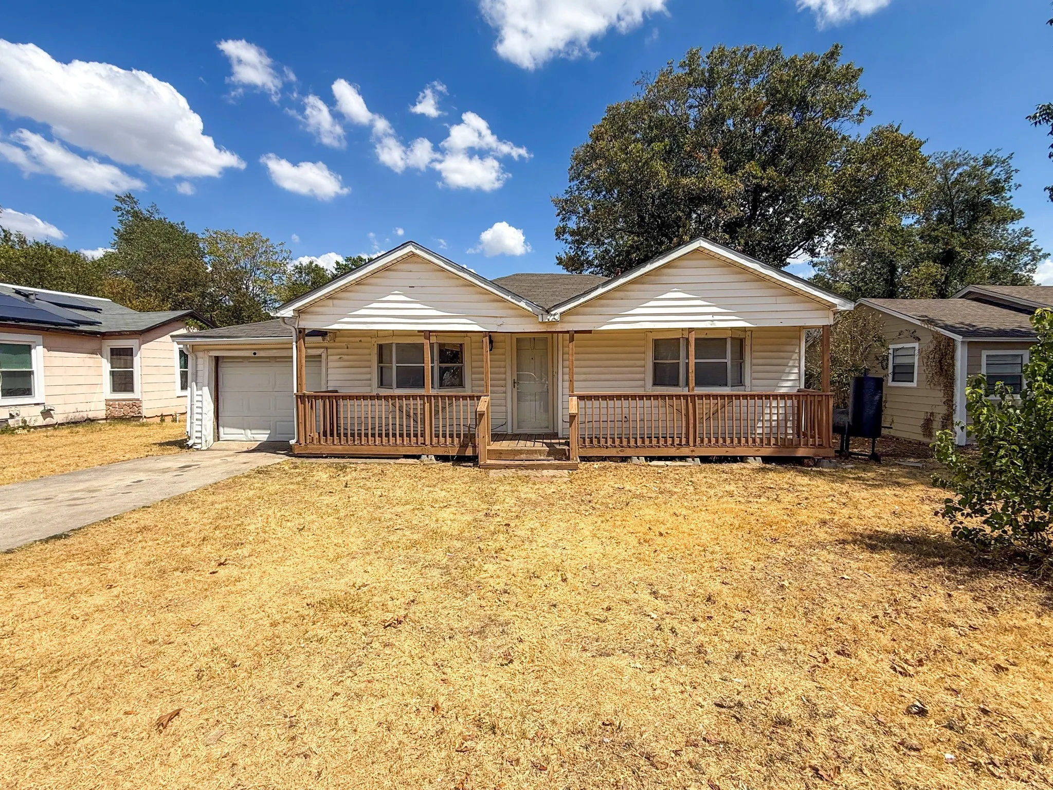 Front facade featuring white siding, a wooden porch with railing, an attached garage, and a concrete driveway