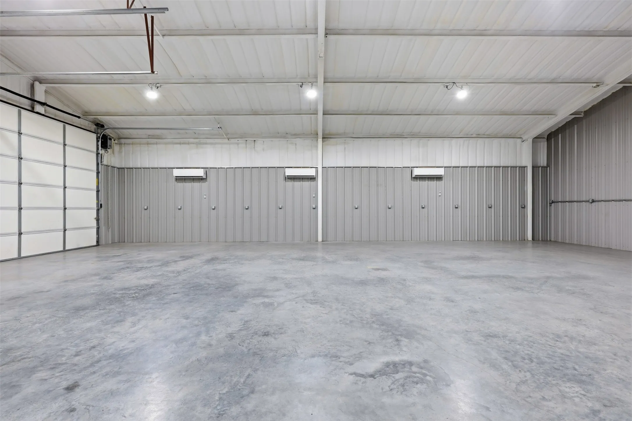 Expansive interior space featuring a concrete floor, high ceilings with exposed beams, recessed lighting, and a large roll-up door