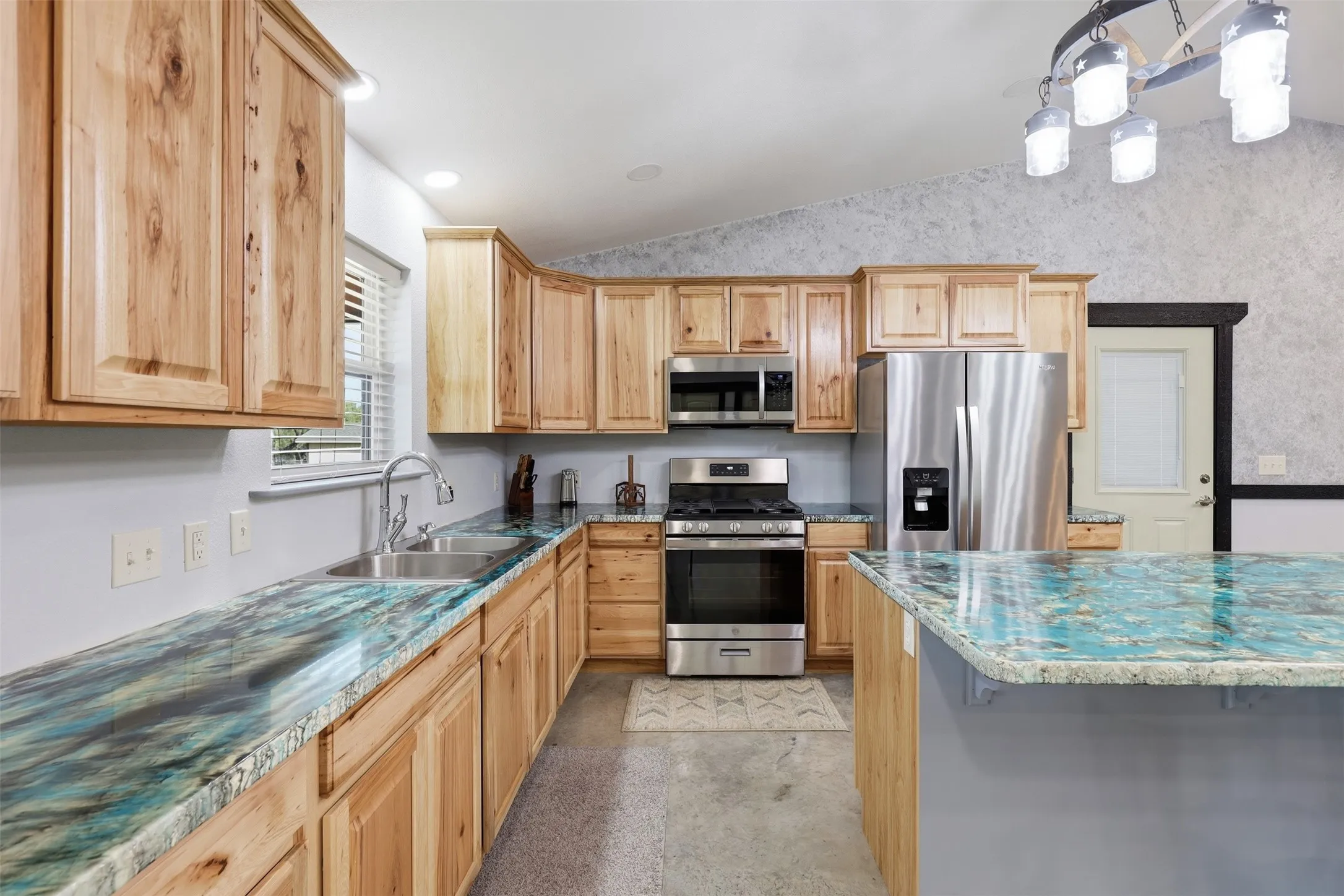 Kitchen featuring natural wood cabinetry, stainless steel appliances, vibrant countertops, an island with seating, and a vaulted ceiling