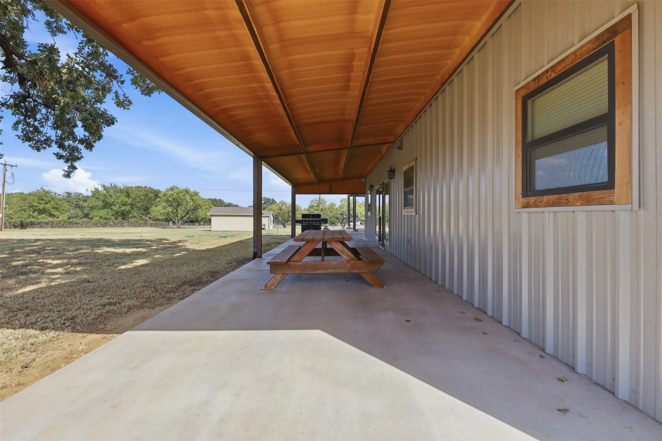 Expansive covered concrete patio with a wood-finish ceiling, flanked by a metal-sided exterior and a window with a wood-trimmed frame