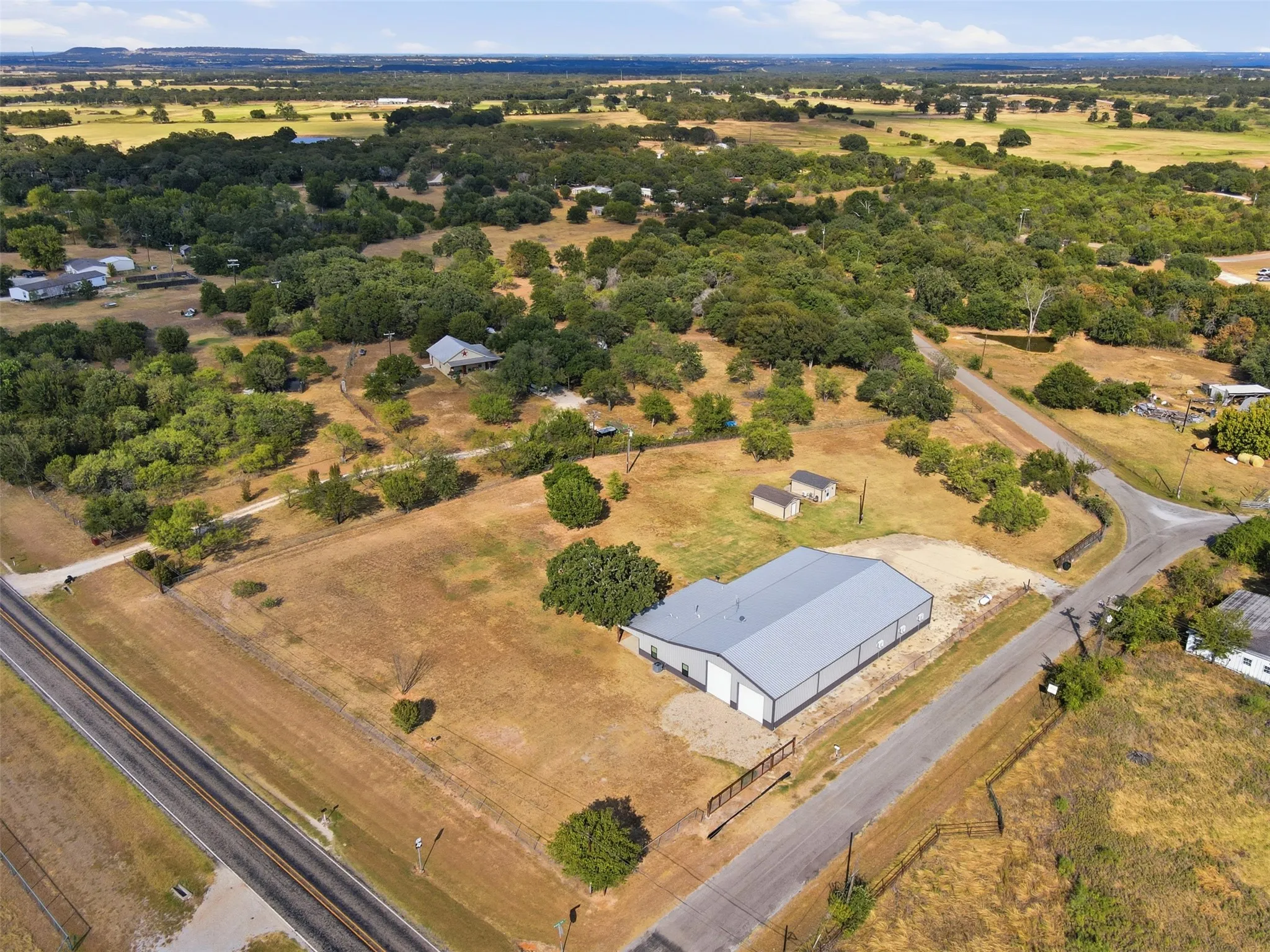 Expansive rural property featuring a large metal building, two smaller outbuildings, and a surrounding landscape of mature trees and open fields